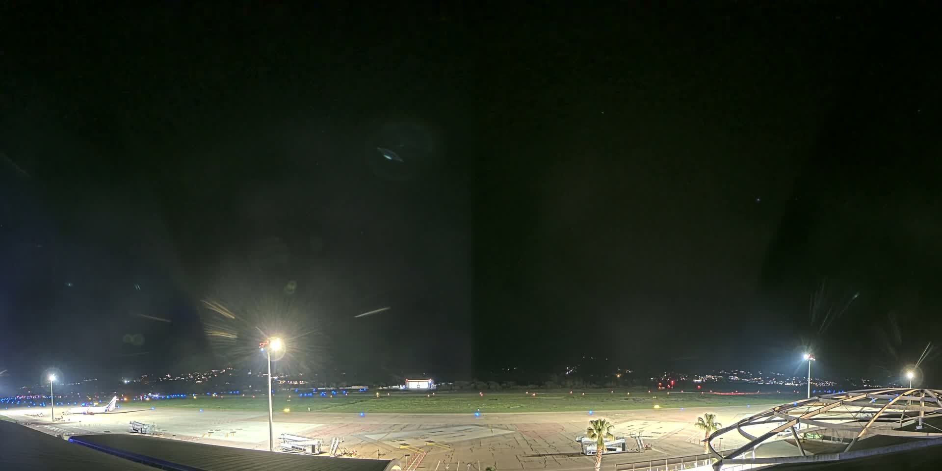 A nighttime view of an airport tarmac with a plane parked near a terminal building under a clear, dark sky.