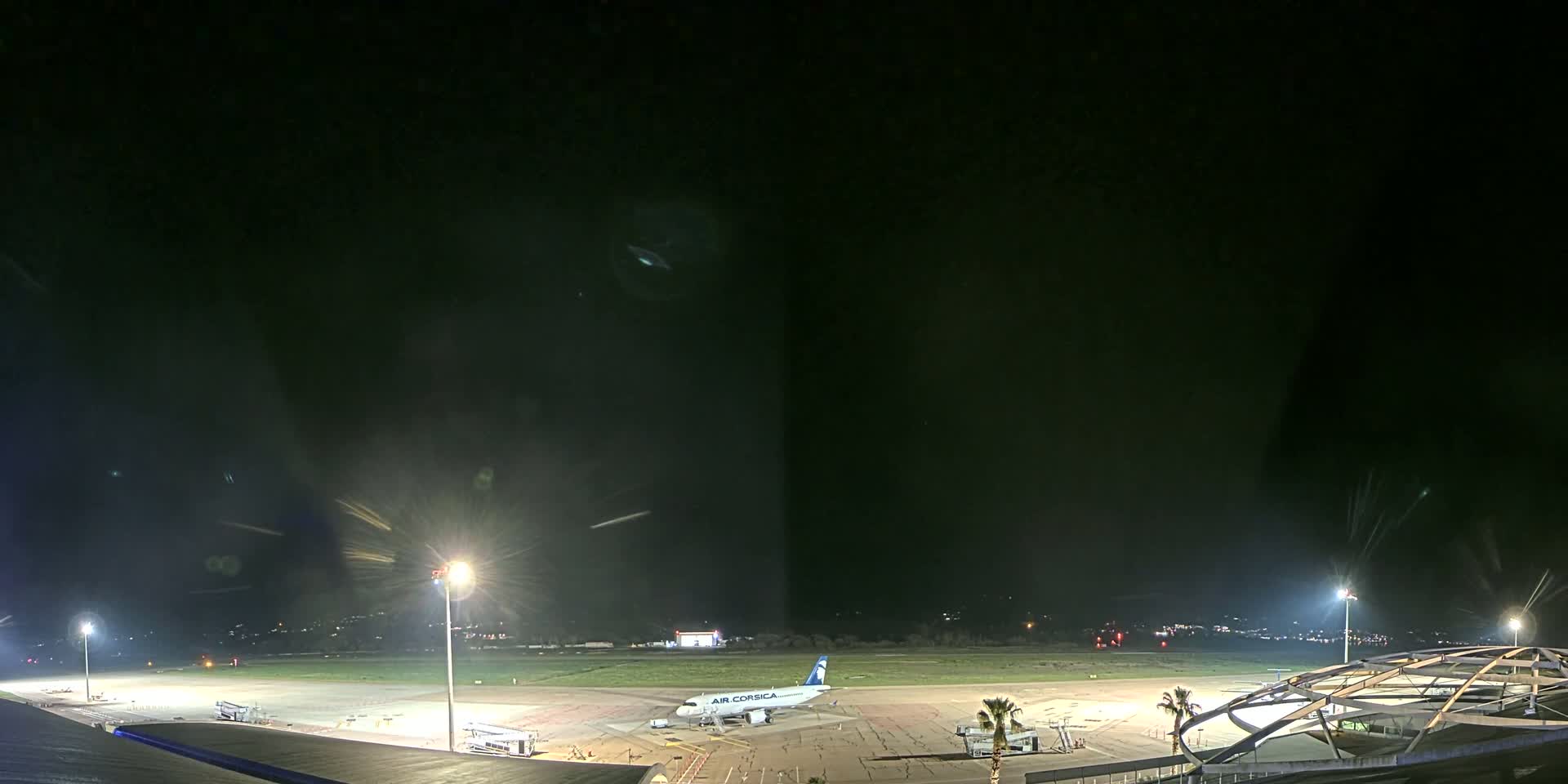 A passenger airplane sits on a tarmac at night under bright lights, with a dark, clear sky above.