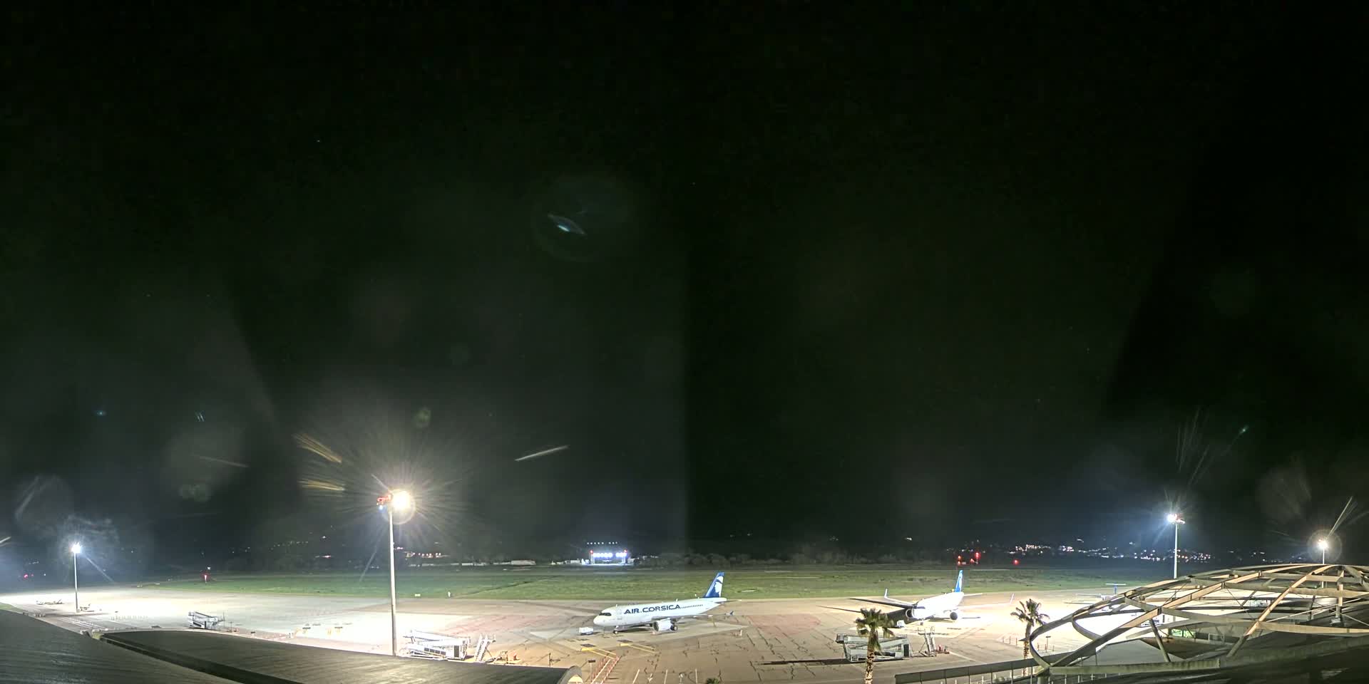 At night, two airplanes are parked on a brightly lit airport tarmac.