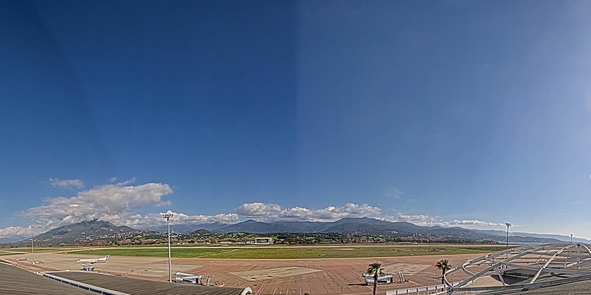 A mostly sunny day at an airport with a view of distant mountains.