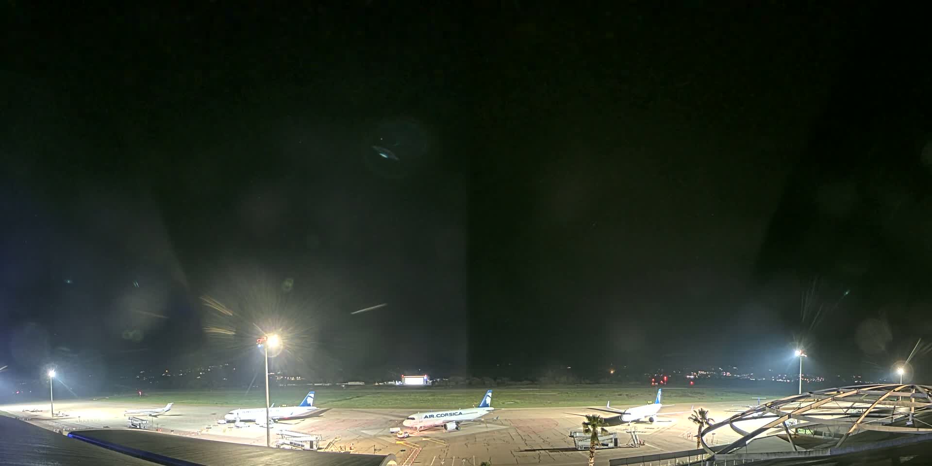 At night, several airplanes are parked on a tarmac illuminated by bright lights, with a dark sky overhead.