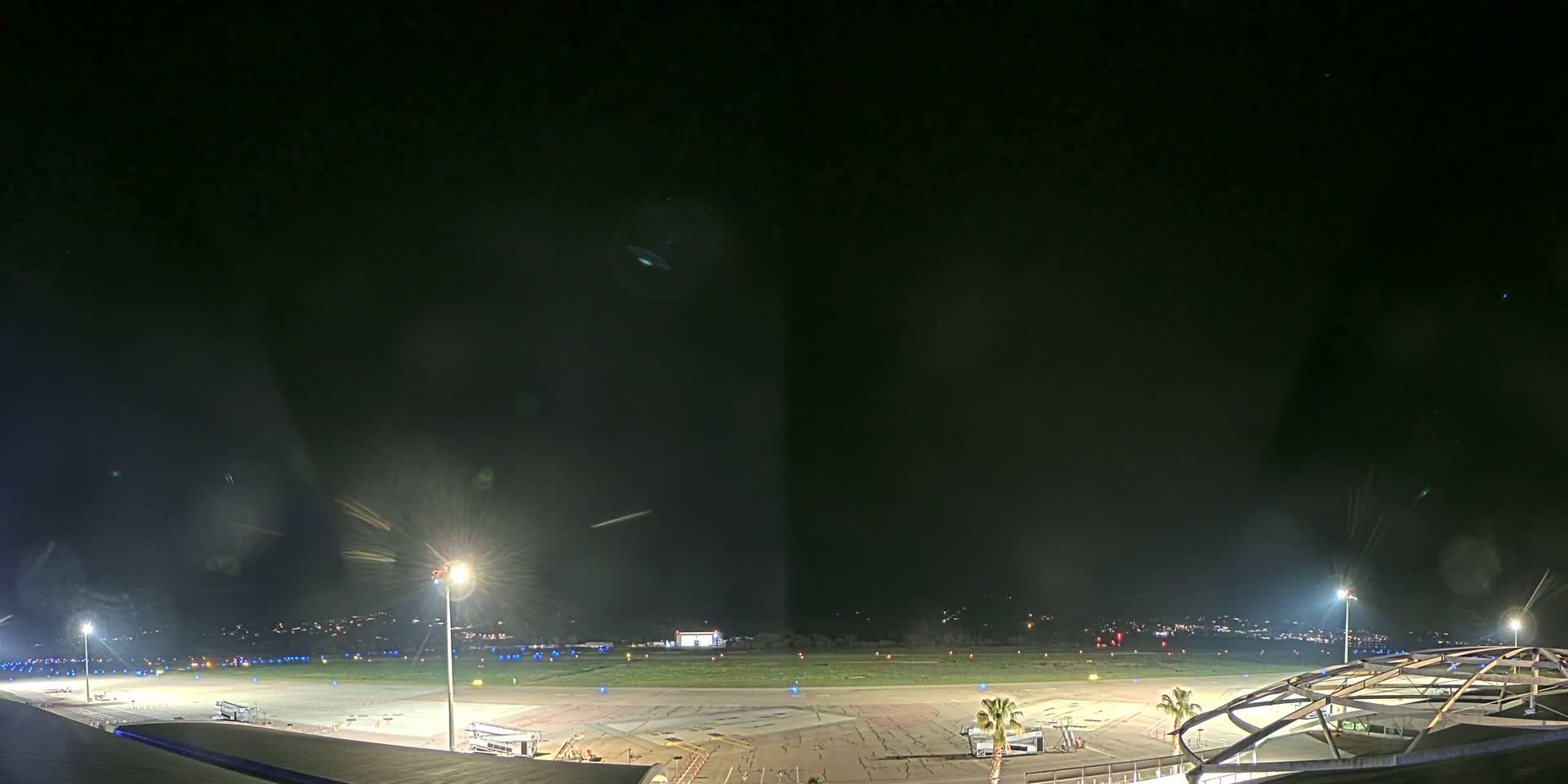 A nighttime view of an airport tarmac, illuminated by bright lights, under a clear, dark sky.