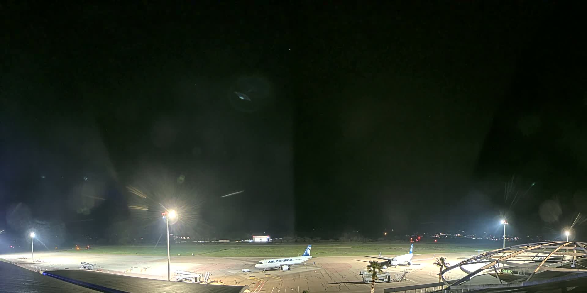 At night, two airplanes are parked on an airport tarmac illuminated by bright lights, under a clear, dark sky.