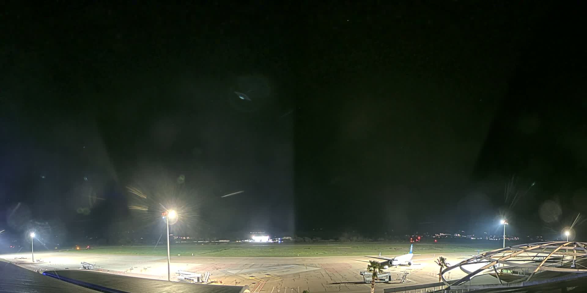 A nighttime view of an airport tarmac with a plane parked near a terminal building under clear skies.