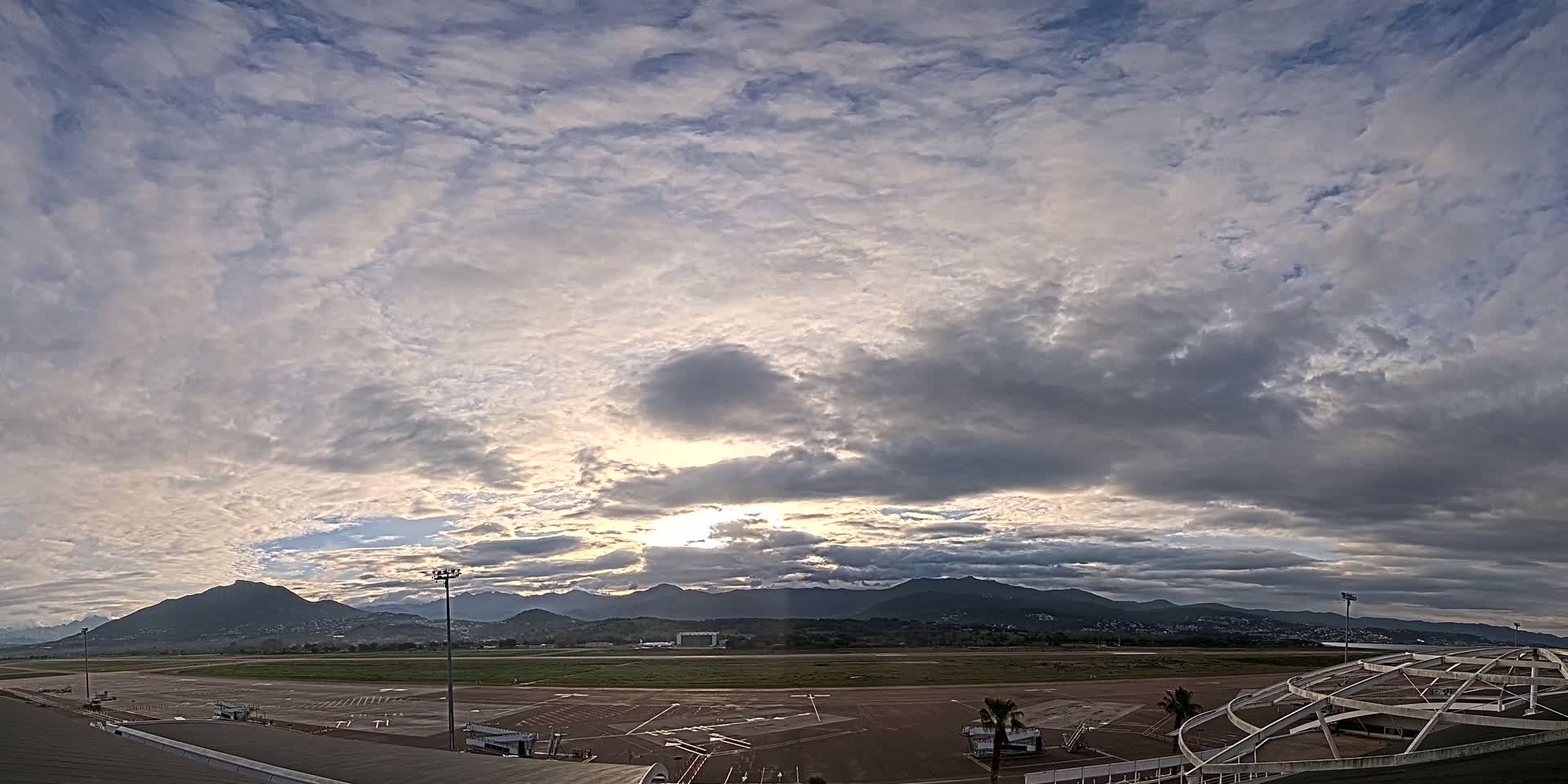 A mostly cloudy sky over an airport runway with mountains in the distance.