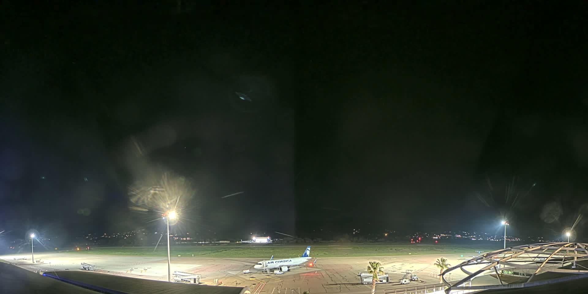 A nighttime view of an airport tarmac with a single airplane parked, illuminated by bright lights under a dark, possibly cloudy sky.