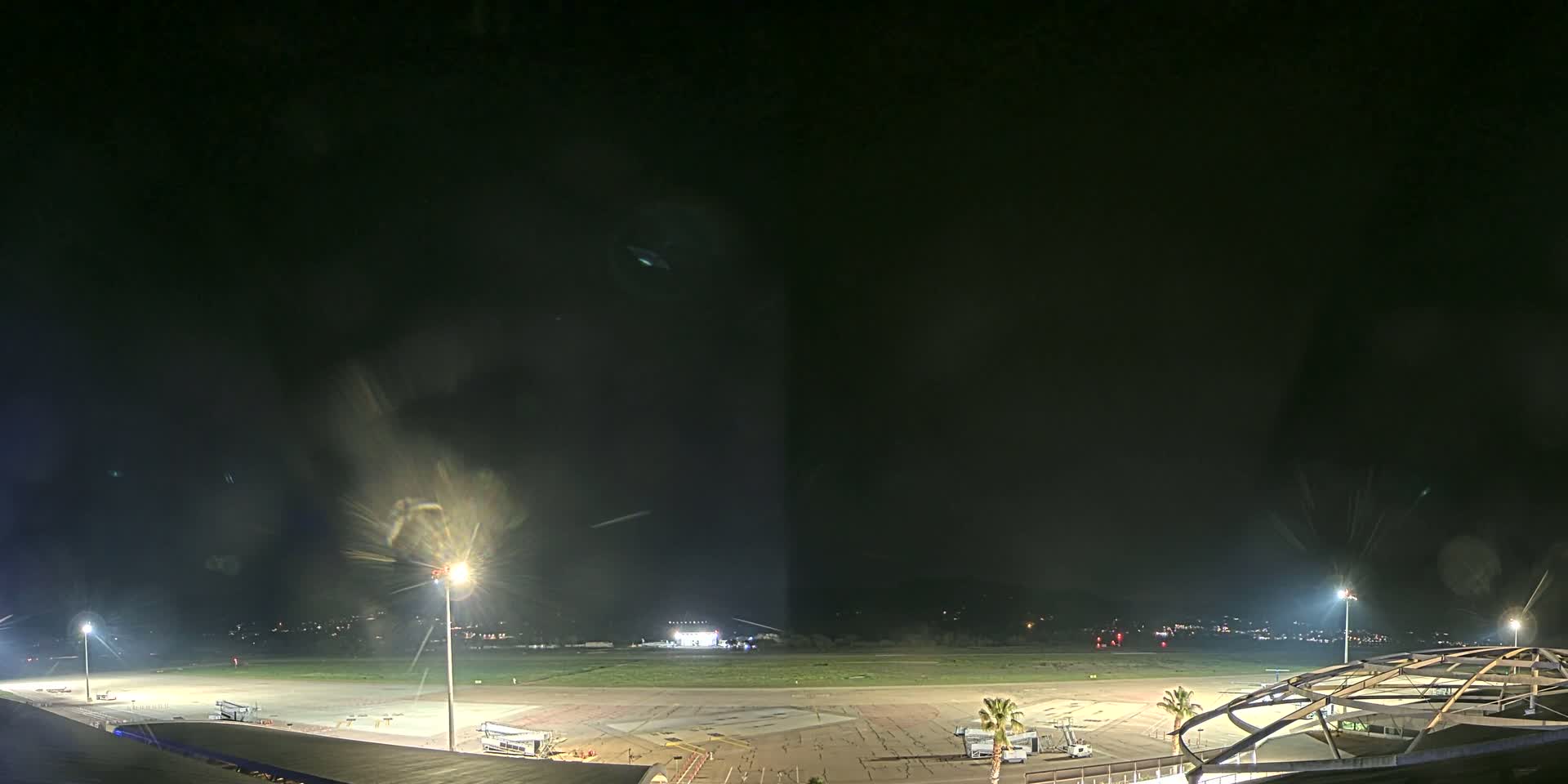 An empty airport tarmac at night is illuminated by several tall lights under a dark, clear sky.