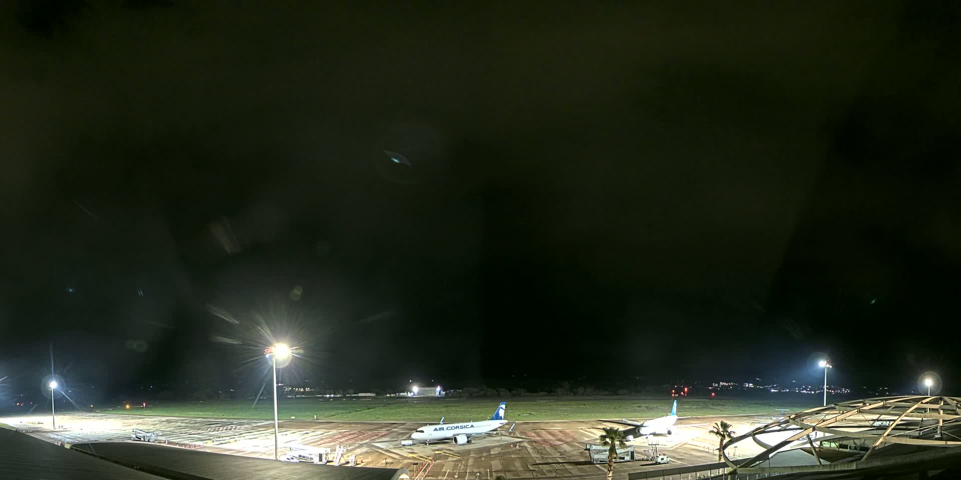 A nighttime view of an airport tarmac with two airplanes parked near a terminal building under a dark, cloudy sky.