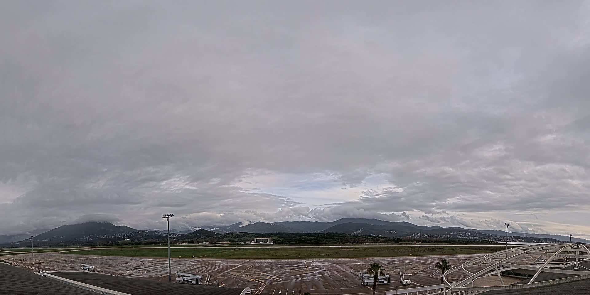 A wet airport tarmac and runway are situated before a range of mountains under a heavily overcast sky.