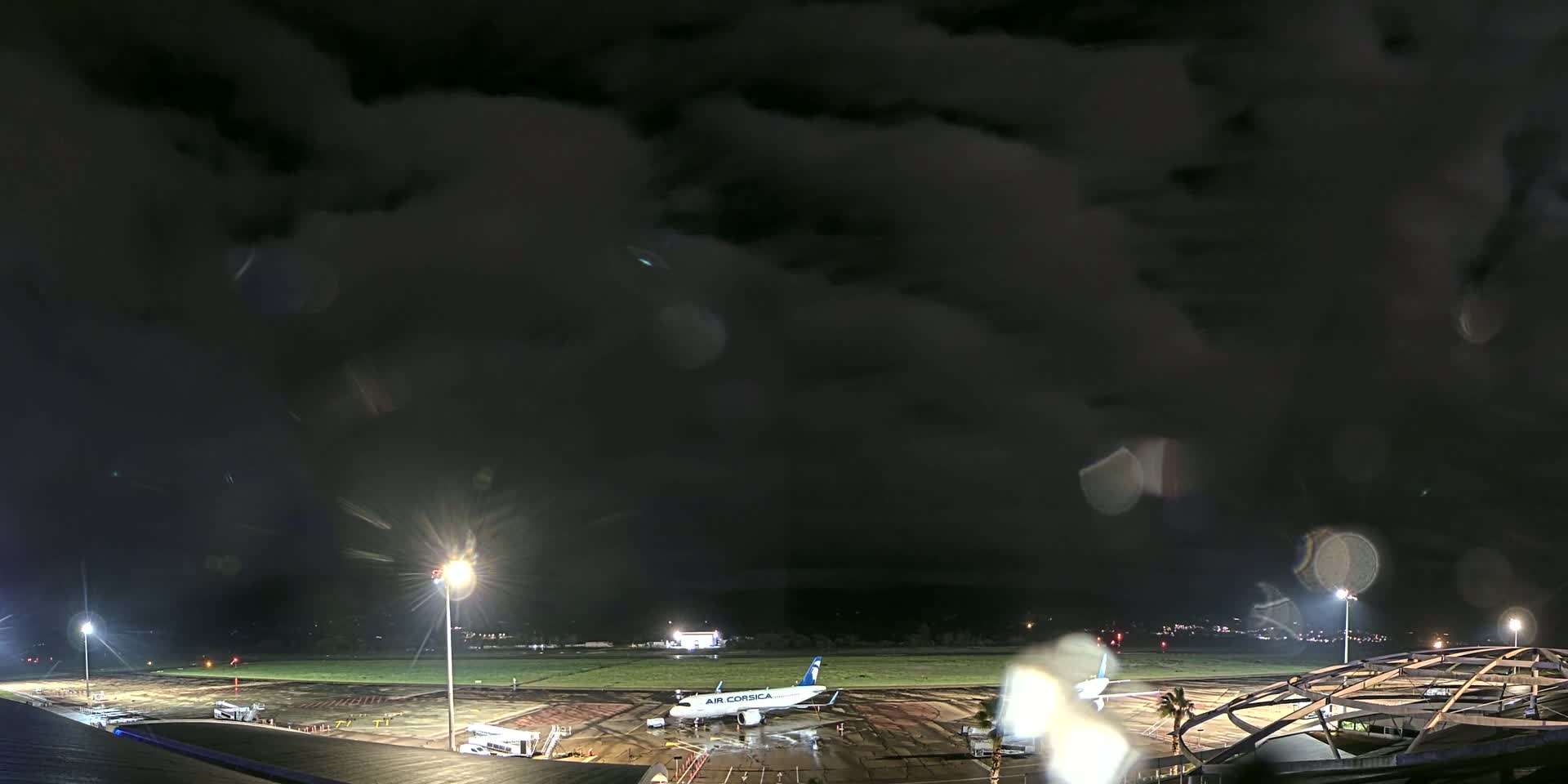 A passenger airplane sits on a rain-slicked tarmac at night under a dark, cloudy sky.