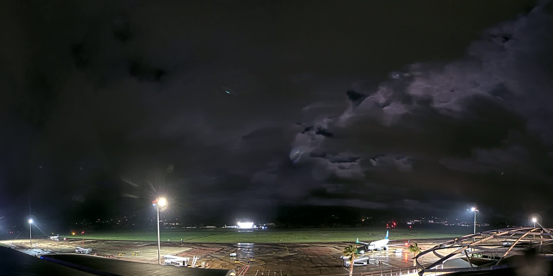 An airplane sits on a rain-slicked airport tarmac at night under a dark, cloudy sky.
