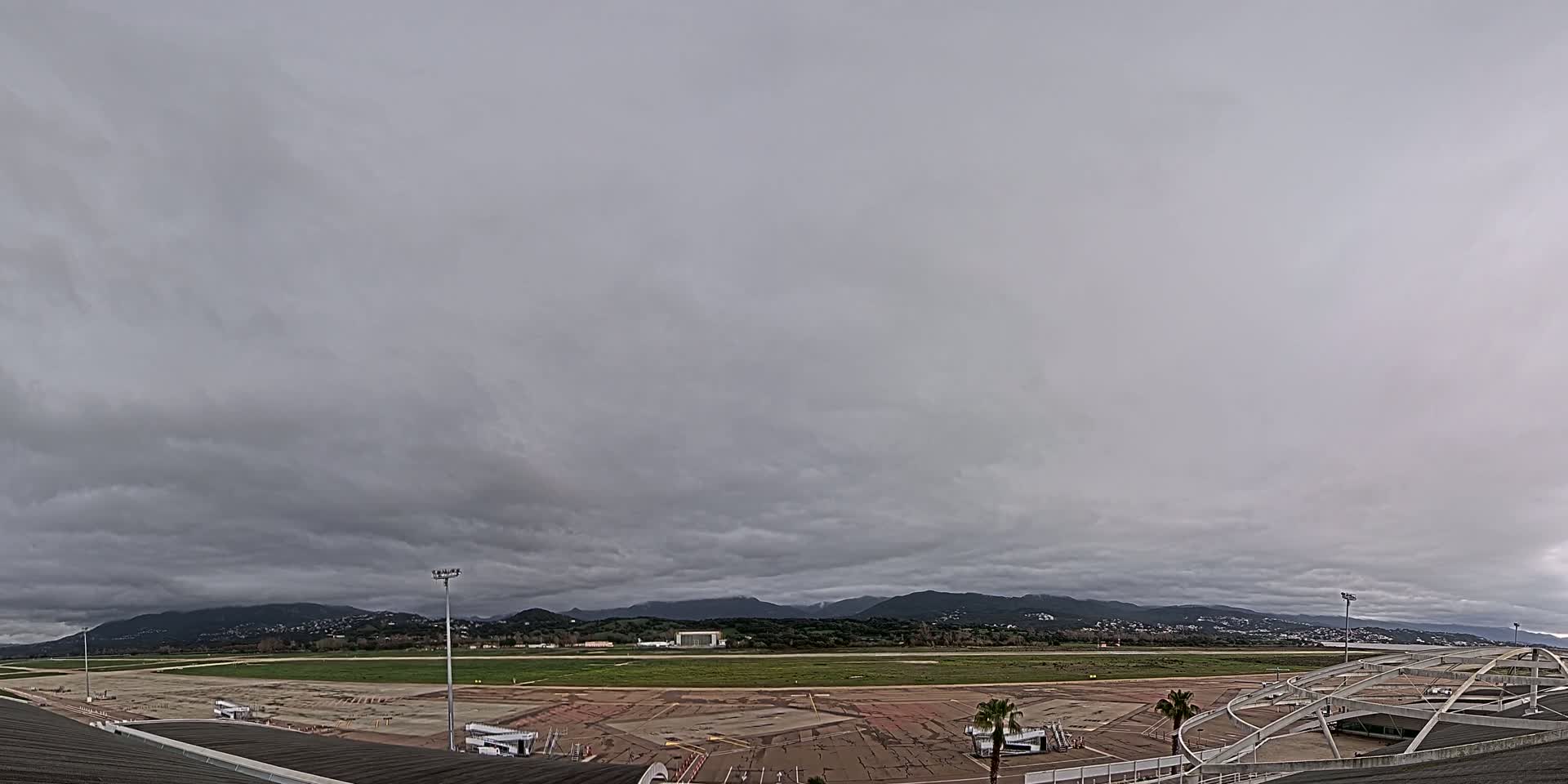 A mostly cloudy sky hangs over an airport tarmac, with mountains visible in the distance.