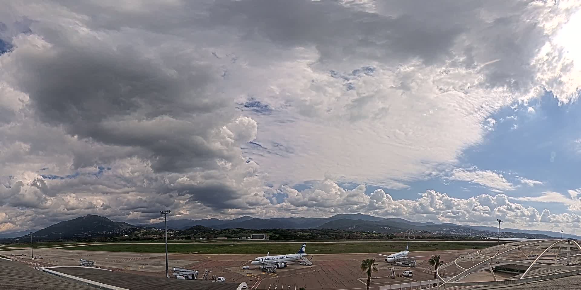 A mostly cloudy sky over an airport tarmac with two airplanes and distant mountains.