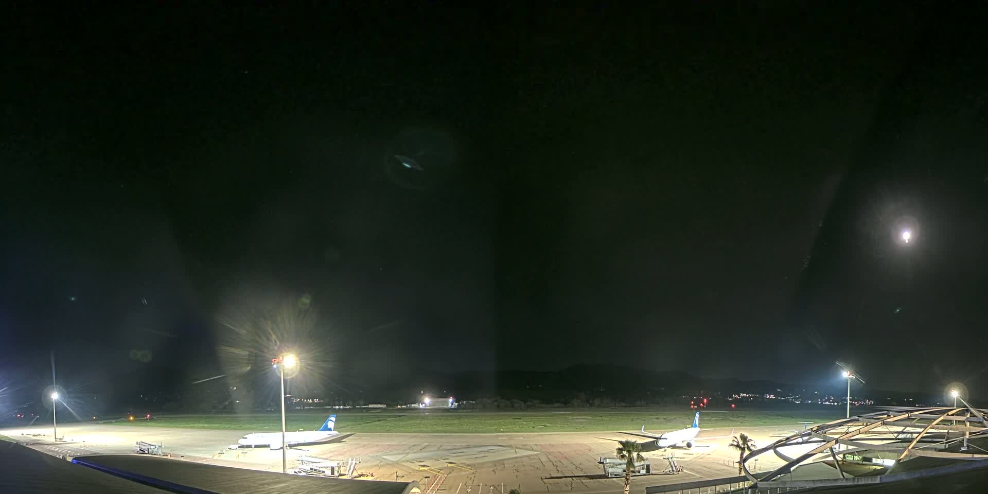 Two airplanes are parked on a brightly lit airport tarmac at night under a clear sky with a bright moon.