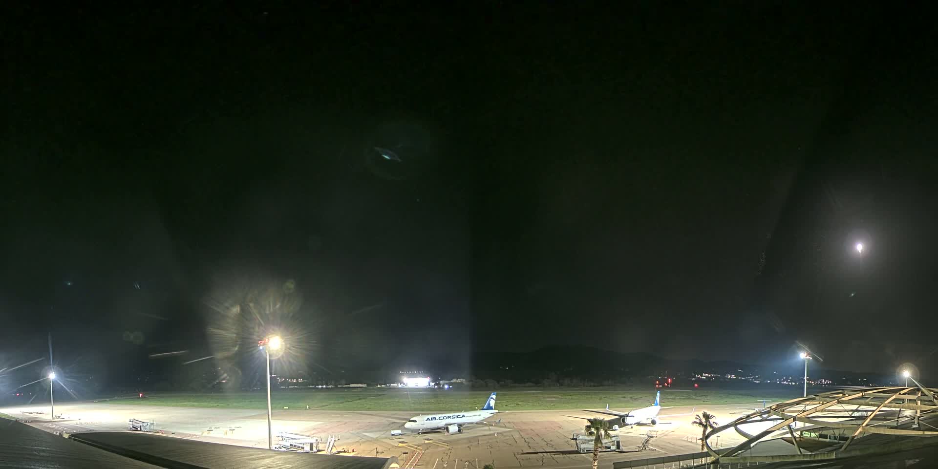 A nighttime view of an airport tarmac with two airplanes parked, illuminated by bright lights under a dark, clear sky.