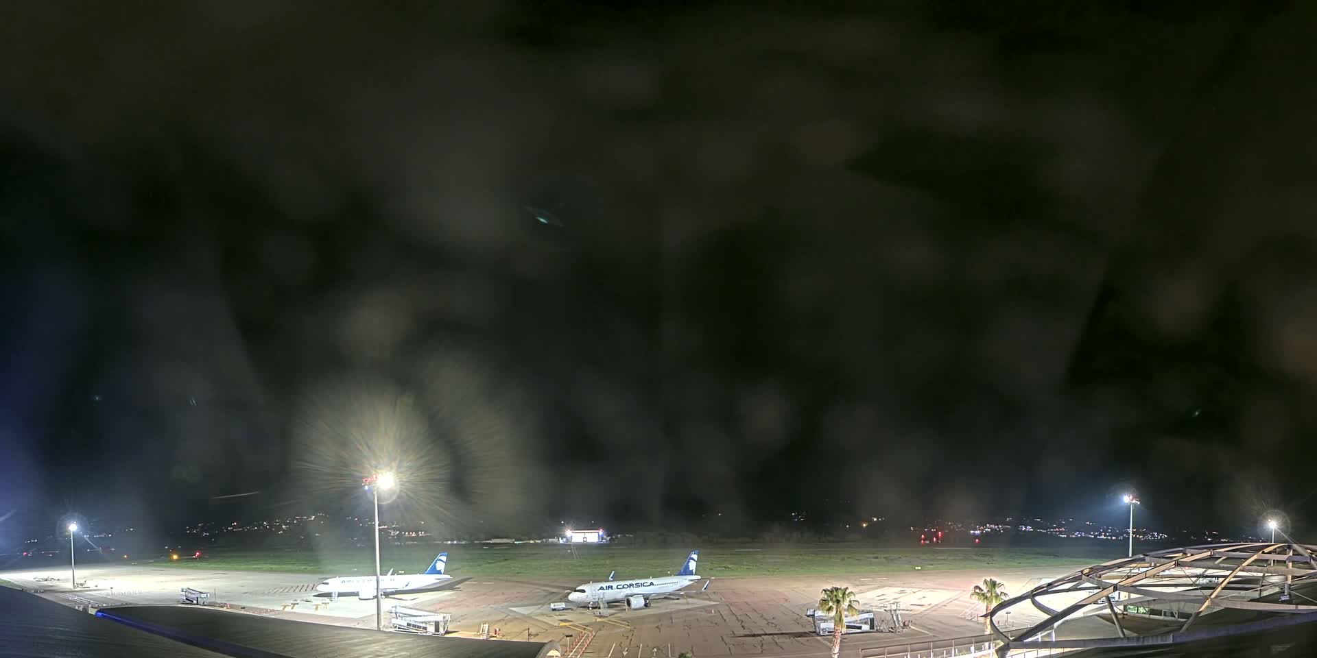 Two airplanes are parked on a dark, rain-swept airport tarmac at night.