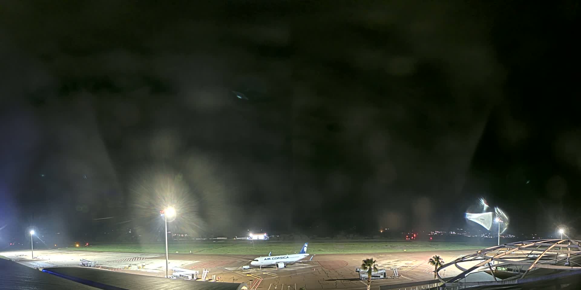 A passenger airplane sits on a tarmac at night under a dark, cloudy sky.