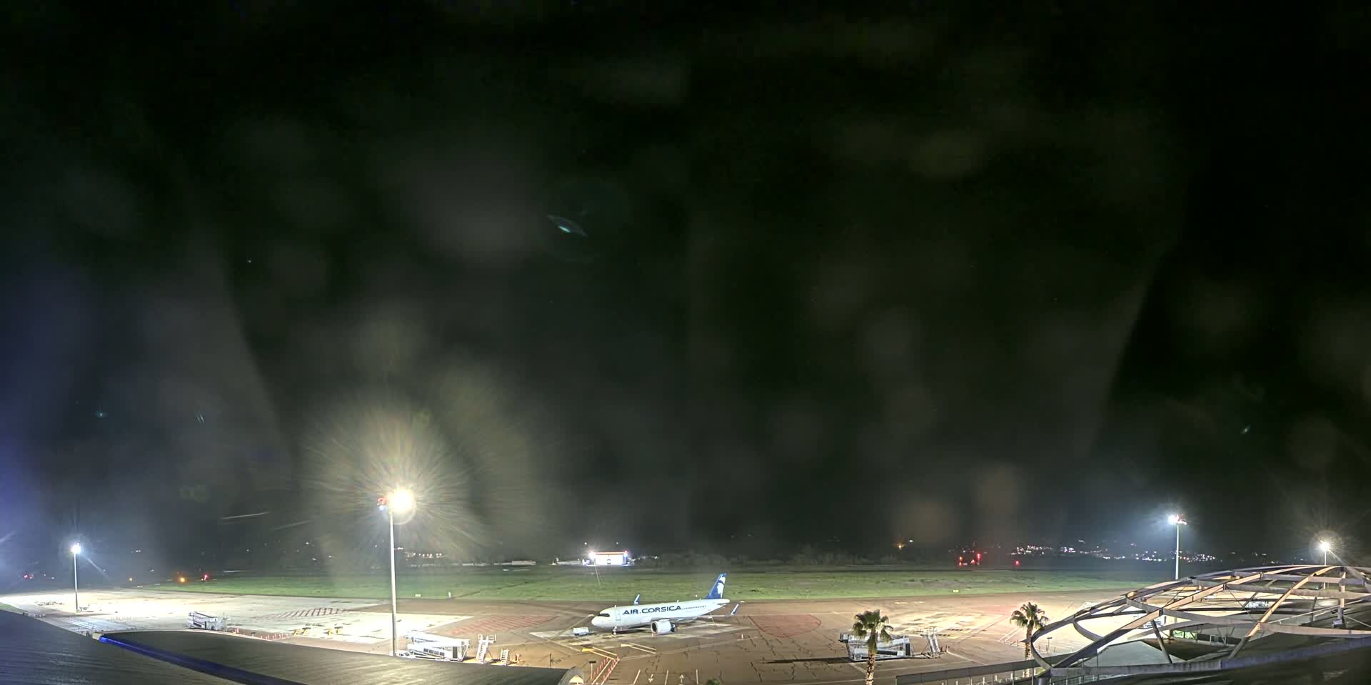 A nighttime view of an airport tarmac with an airplane and airport structures, under hazy or foggy conditions.