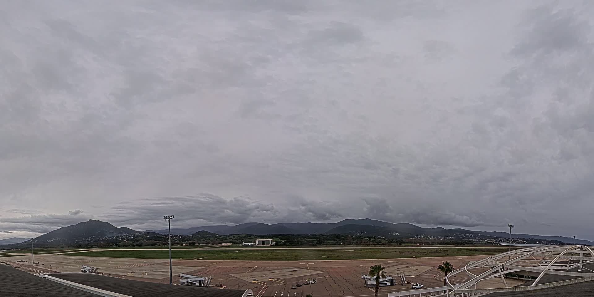 A mostly cloudy sky hangs over an airport tarmac, with distant mountains visible in the background.