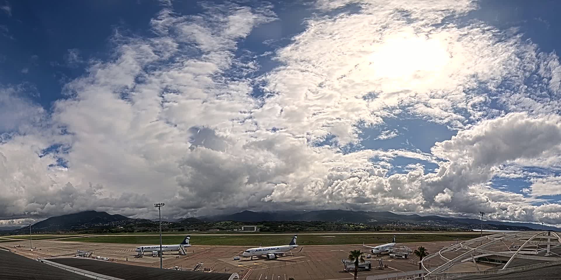 A partly sunny sky with fluffy clouds over an airport tarmac where several airplanes are parked.