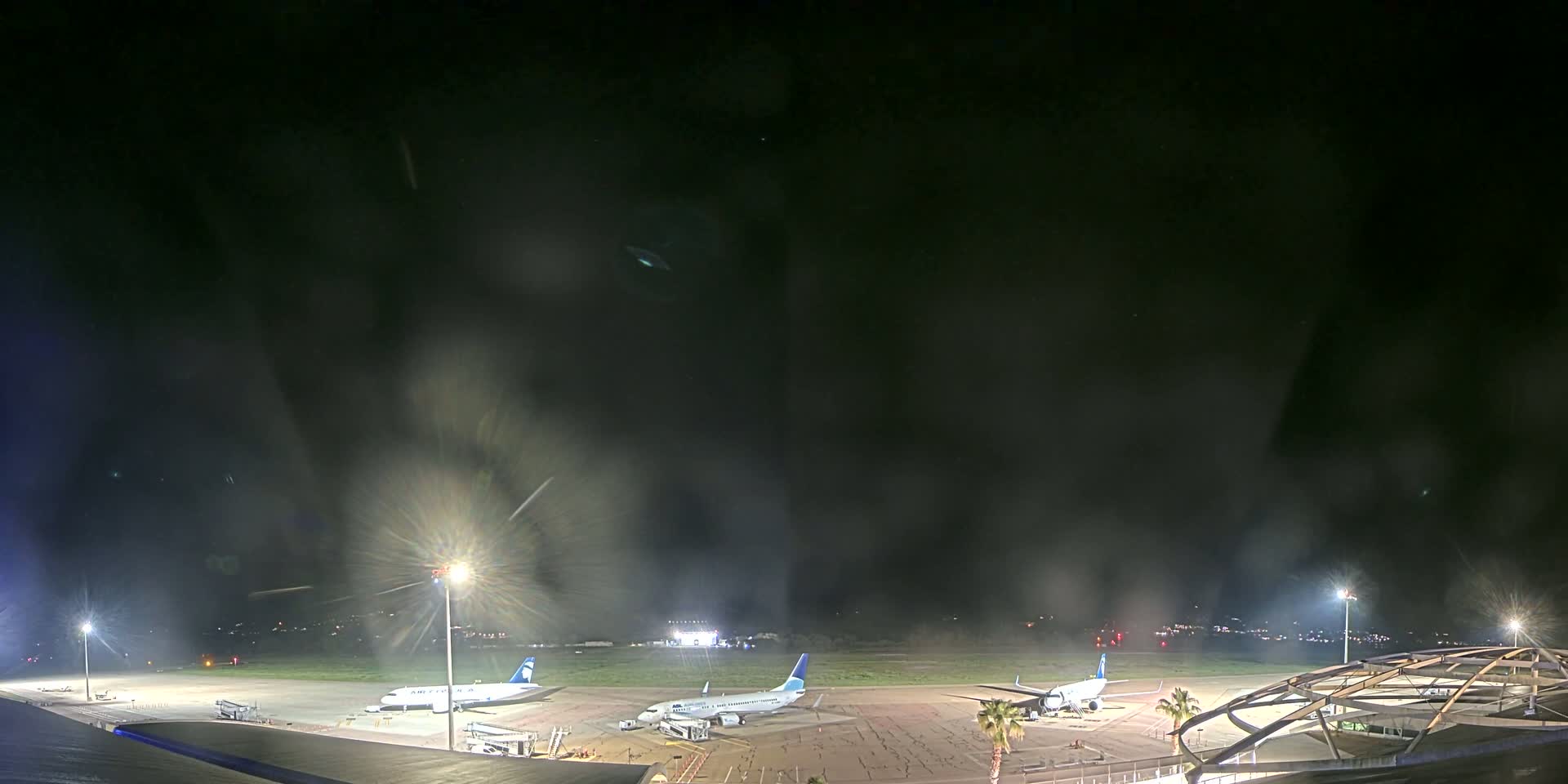 Three airplanes are parked on a dark airport tarmac at night under a hazy sky.