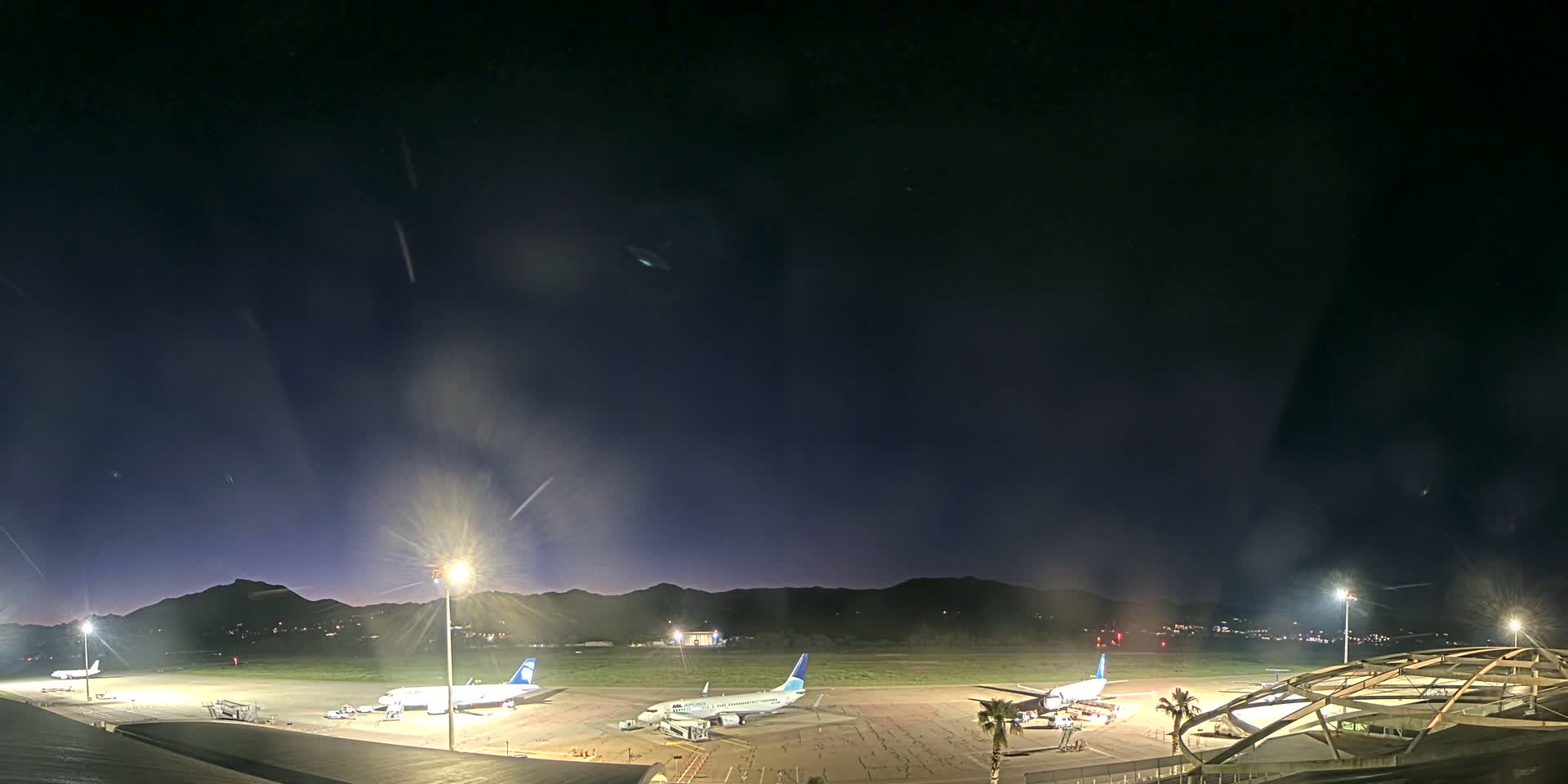 Several airplanes are parked on a dark airport tarmac at night under a mostly clear sky.