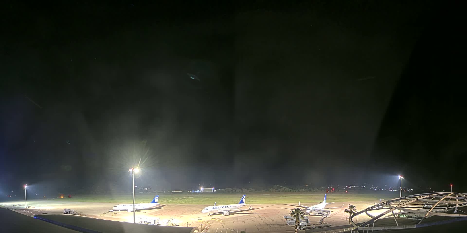 Three airplanes are parked on a brightly lit tarmac at night under a dark, hazy sky.