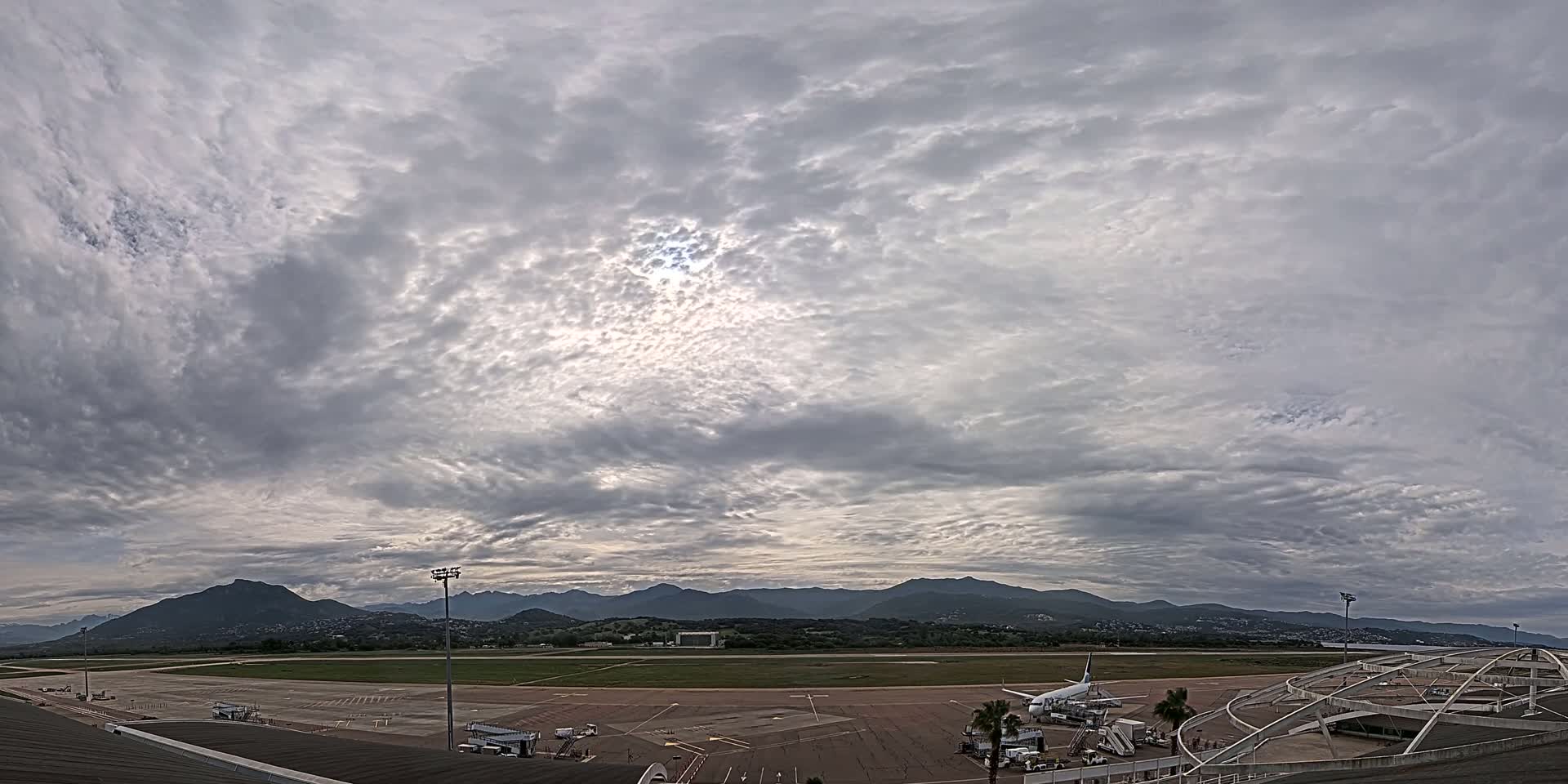 A mostly cloudy sky over an airport tarmac with a large airplane and distant mountains.