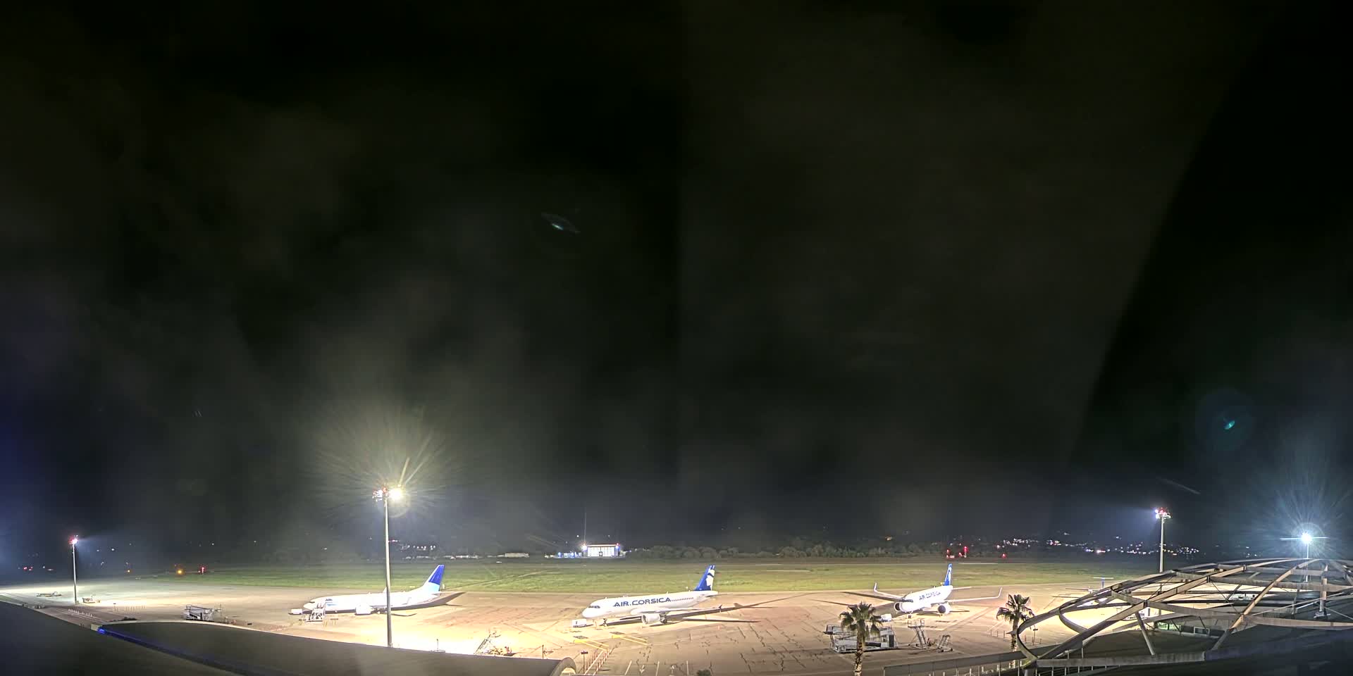 Three airplanes are parked on a dark, brightly lit airport tarmac at night under a hazy sky.