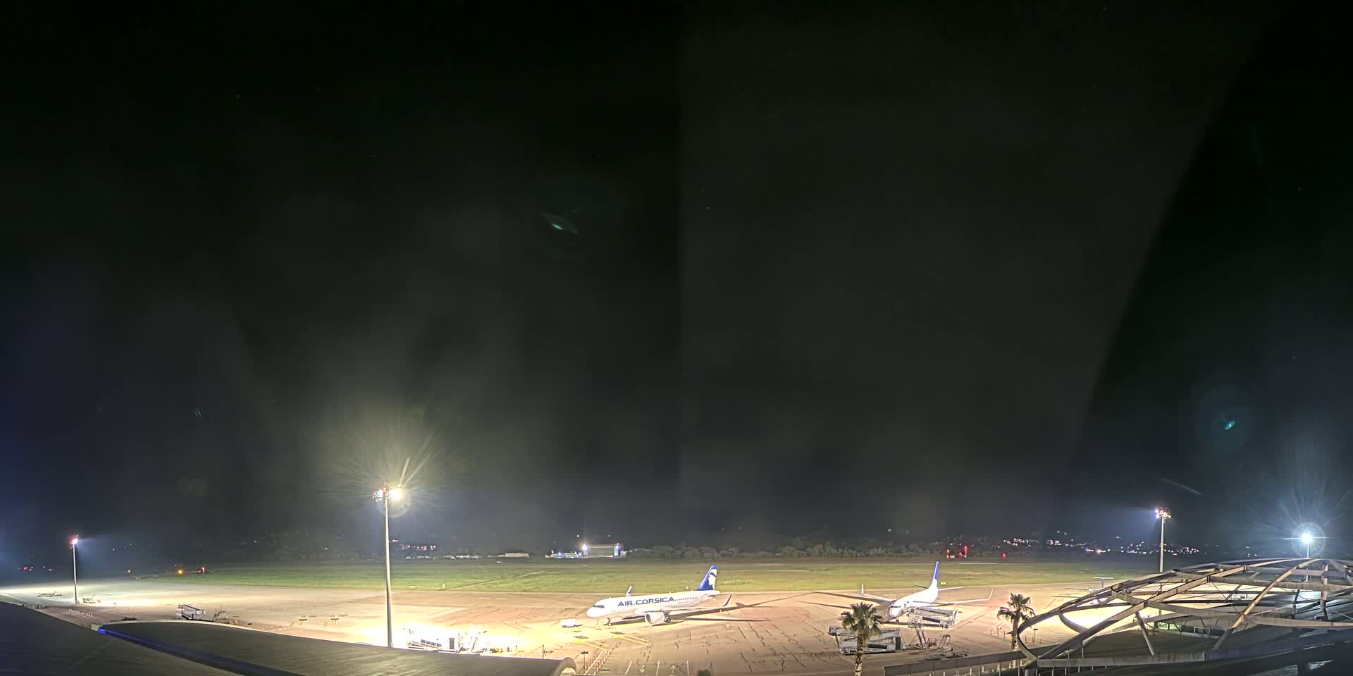 At night, under a dark sky, several airplanes are parked on a brightly lit tarmac at an airport.