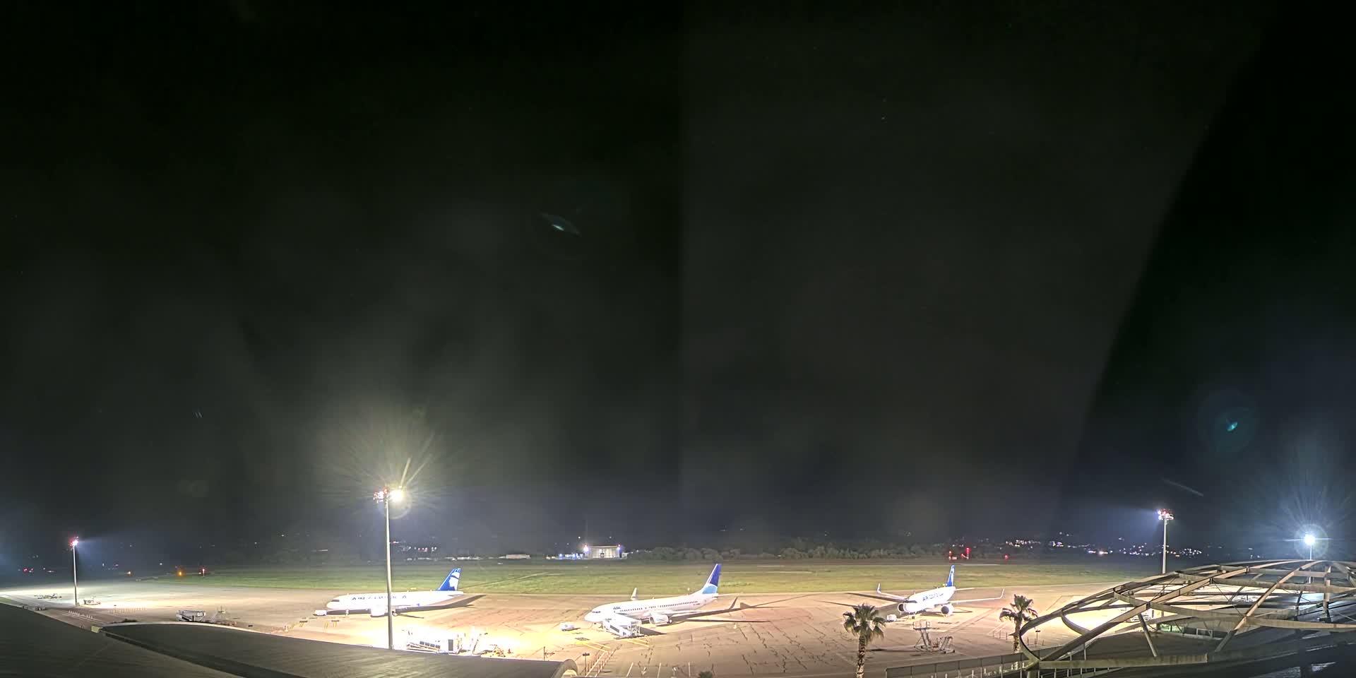 Three airplanes are parked on a dark airport tarmac at night under bright lights.