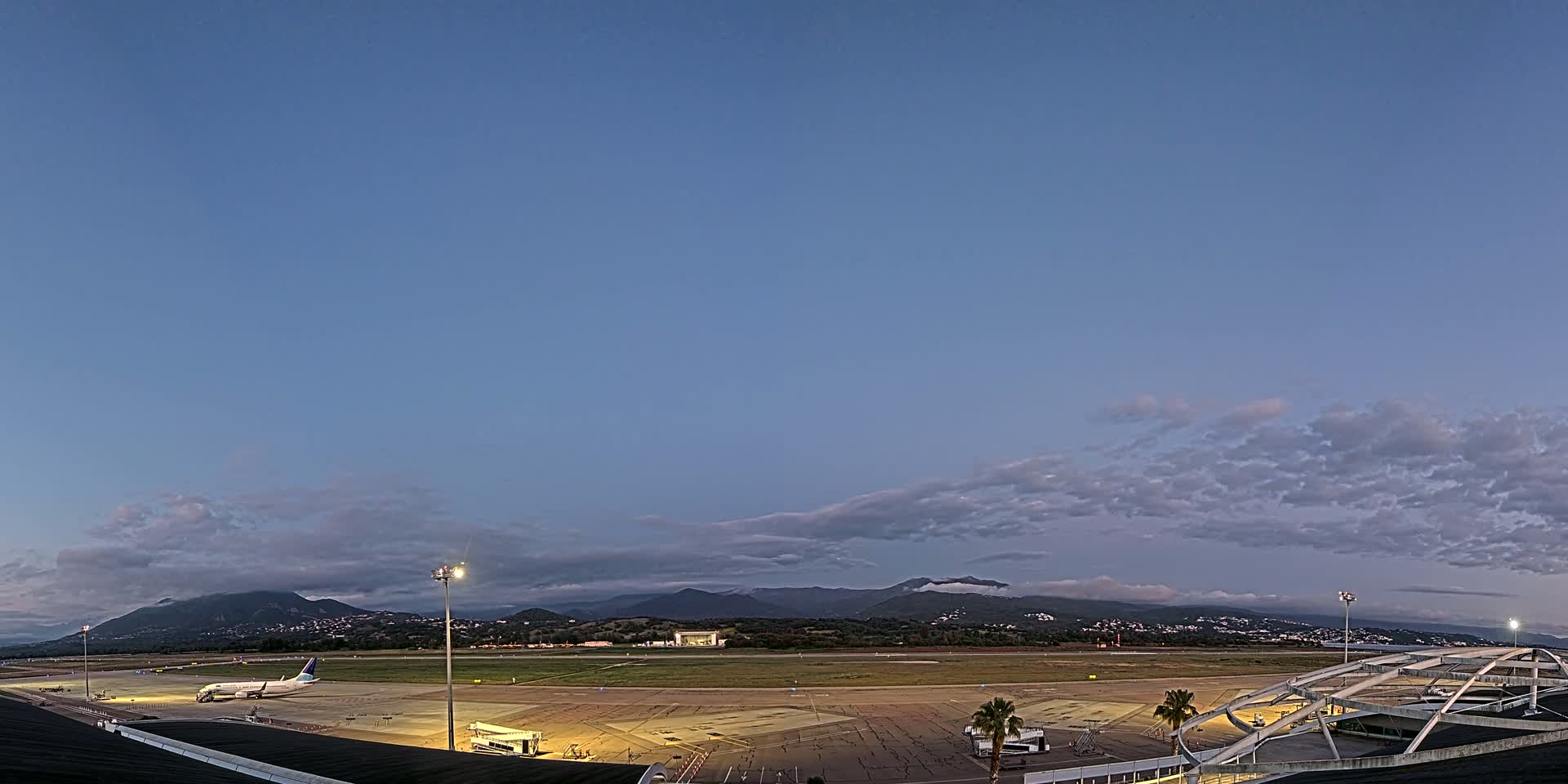 A mostly clear twilight sky over an airport tarmac with a single airplane and mountains in the distance.