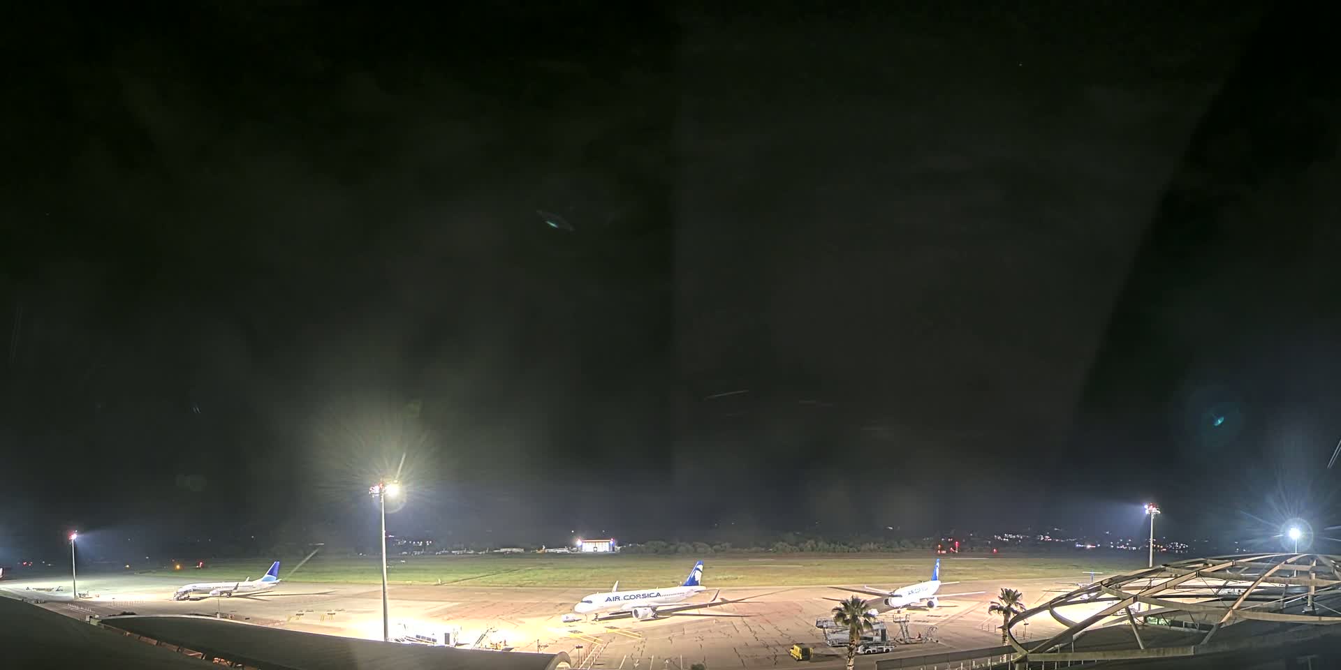 At night, several airplanes are parked on a brightly lit airport tarmac under a dark, cloudy sky.