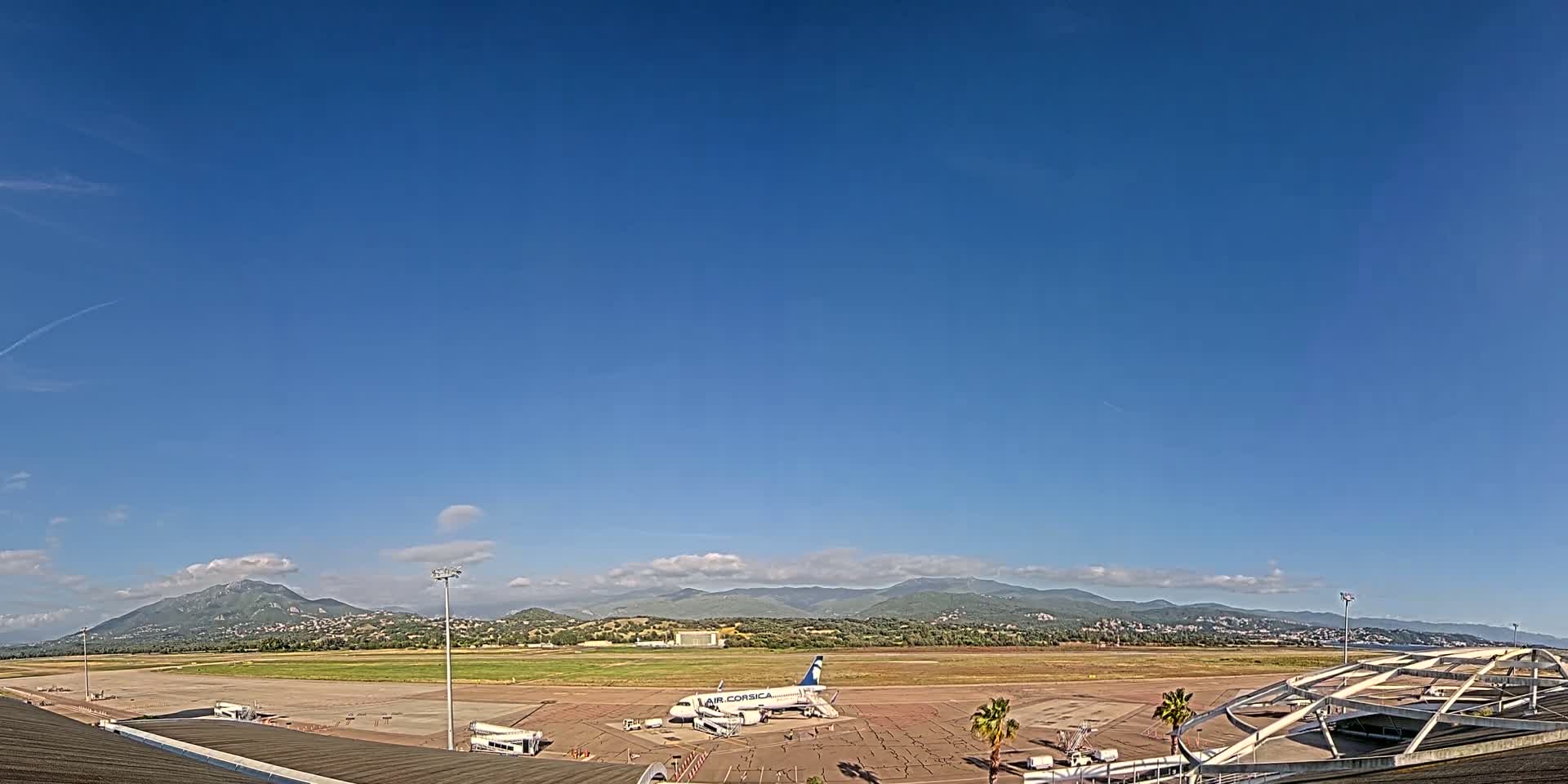 A mostly clear blue sky overlooks an airport tarmac with a single airplane and distant mountains.