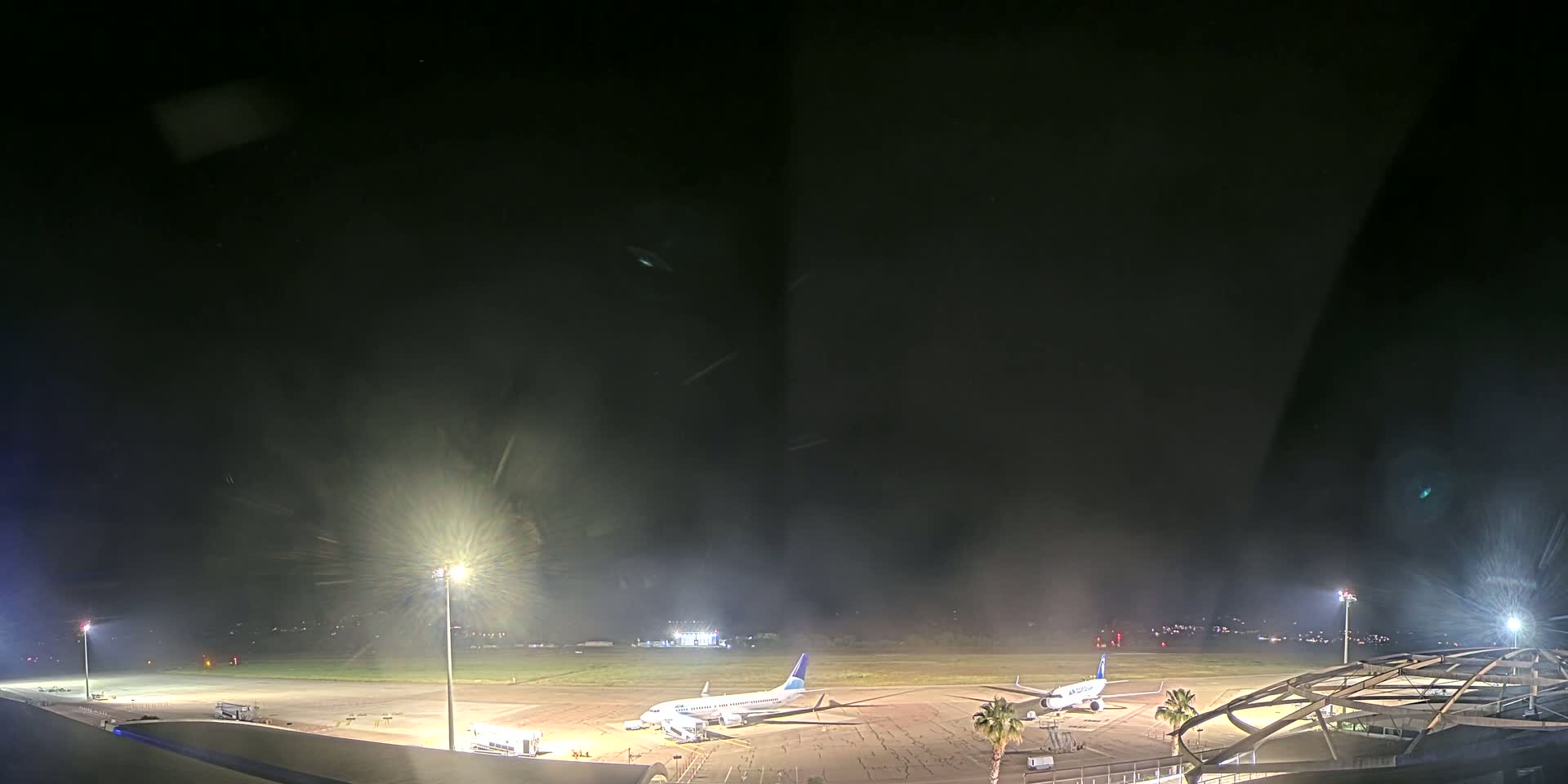 Two airplanes are parked on an airport tarmac at night under hazy conditions.