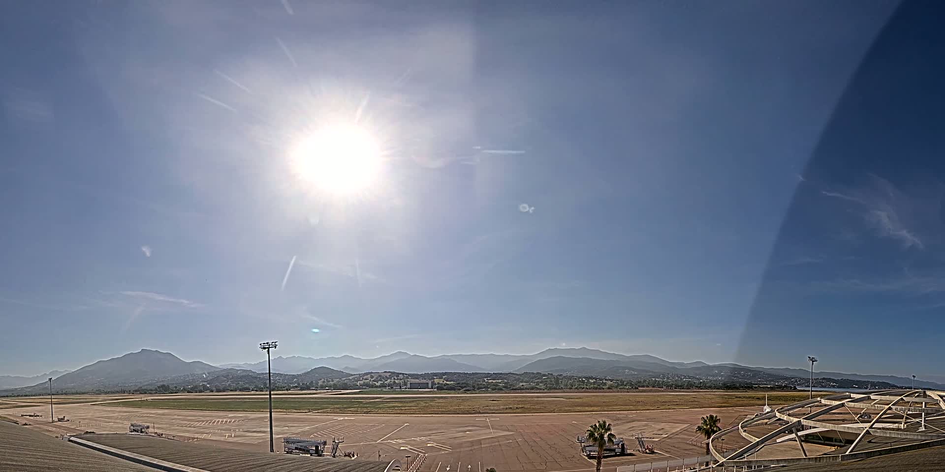 A sunny day at an airport with a runway, parking lot, and distant mountains.