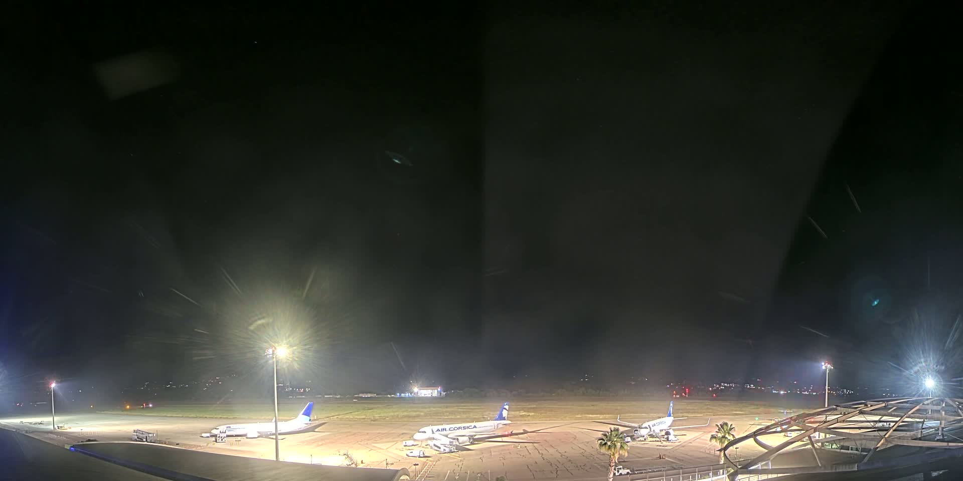 At night, three airplanes are parked on a tarmac at an airport under a dark, slightly hazy sky.