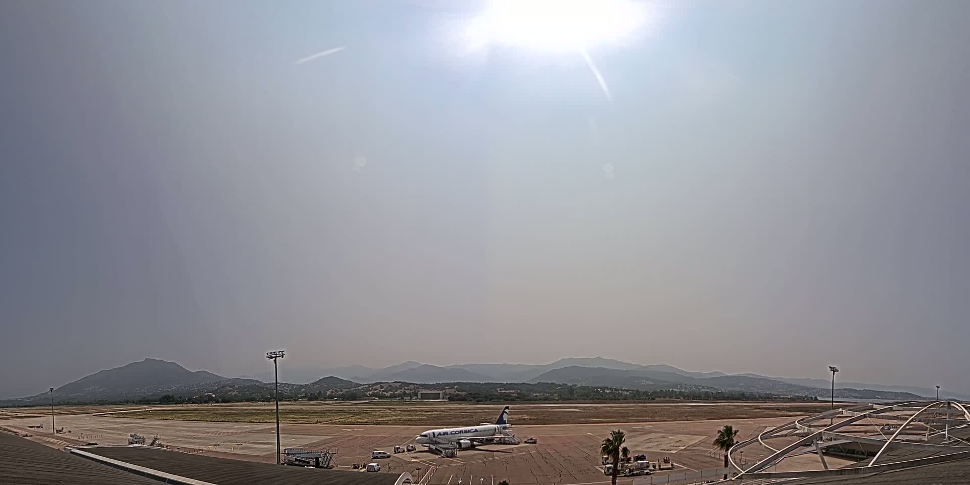 A hazy, sunny day reveals an airplane on the tarmac of an airport, backed by a range of distant mountains.