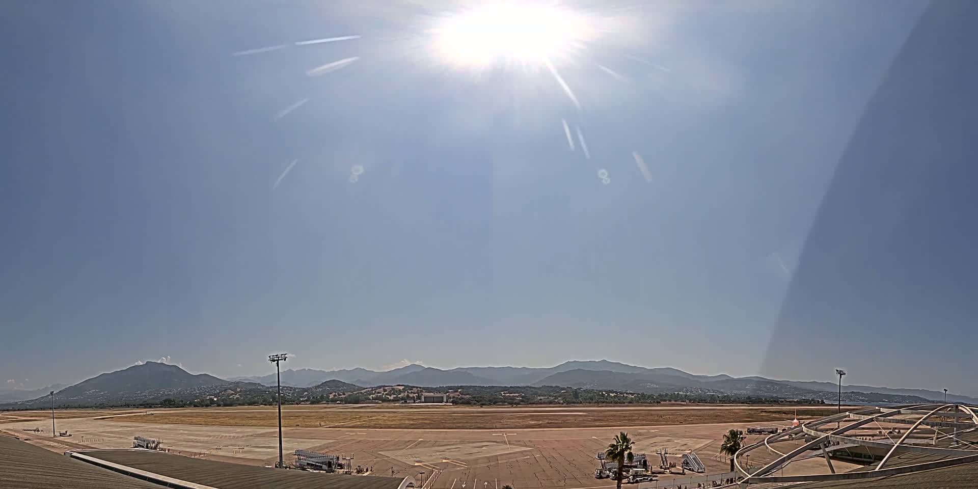 A sunny day reveals an airport tarmac with a distant mountain range under a mostly clear sky.