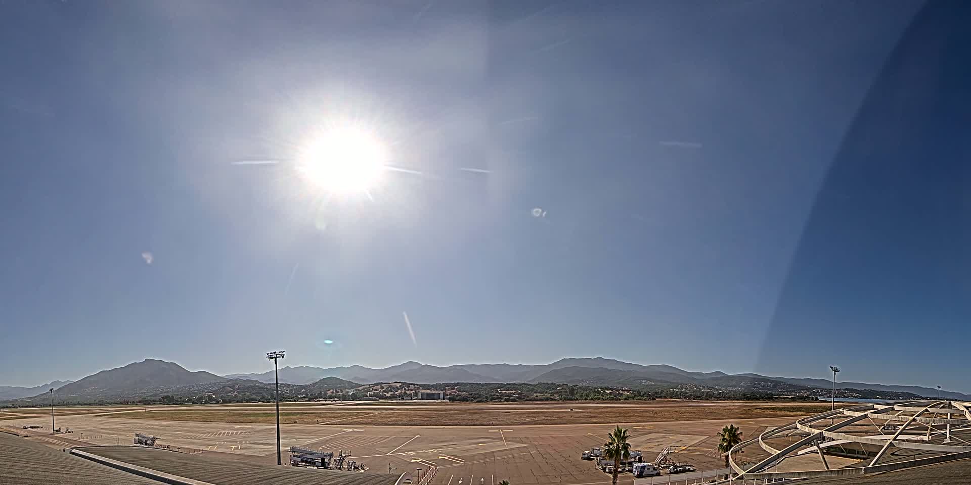 A sunny day at an airport with a runway and tarmac, backed by distant mountains.