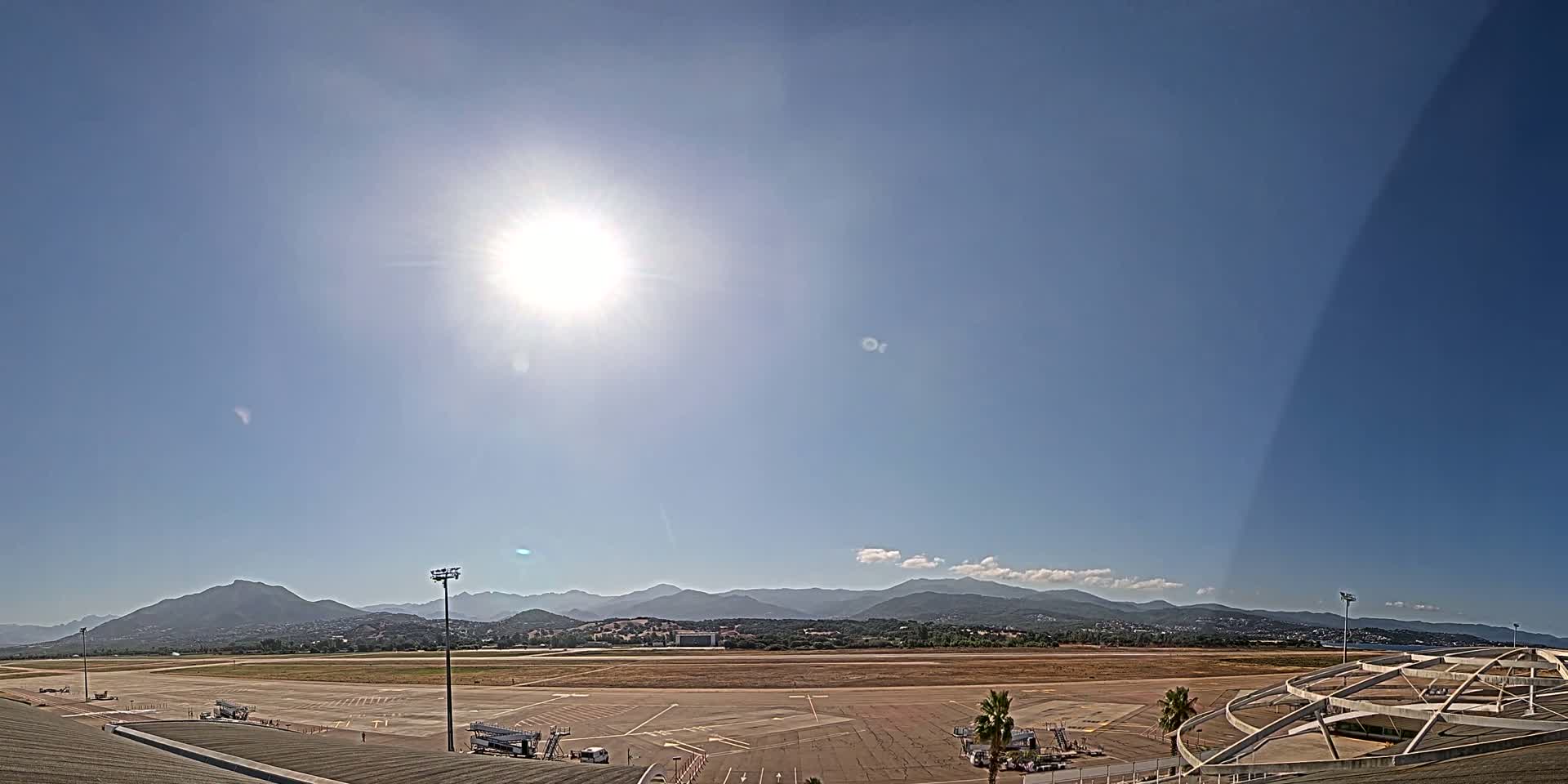 A sunny day reveals a mostly empty airport tarmac with mountains in the background.