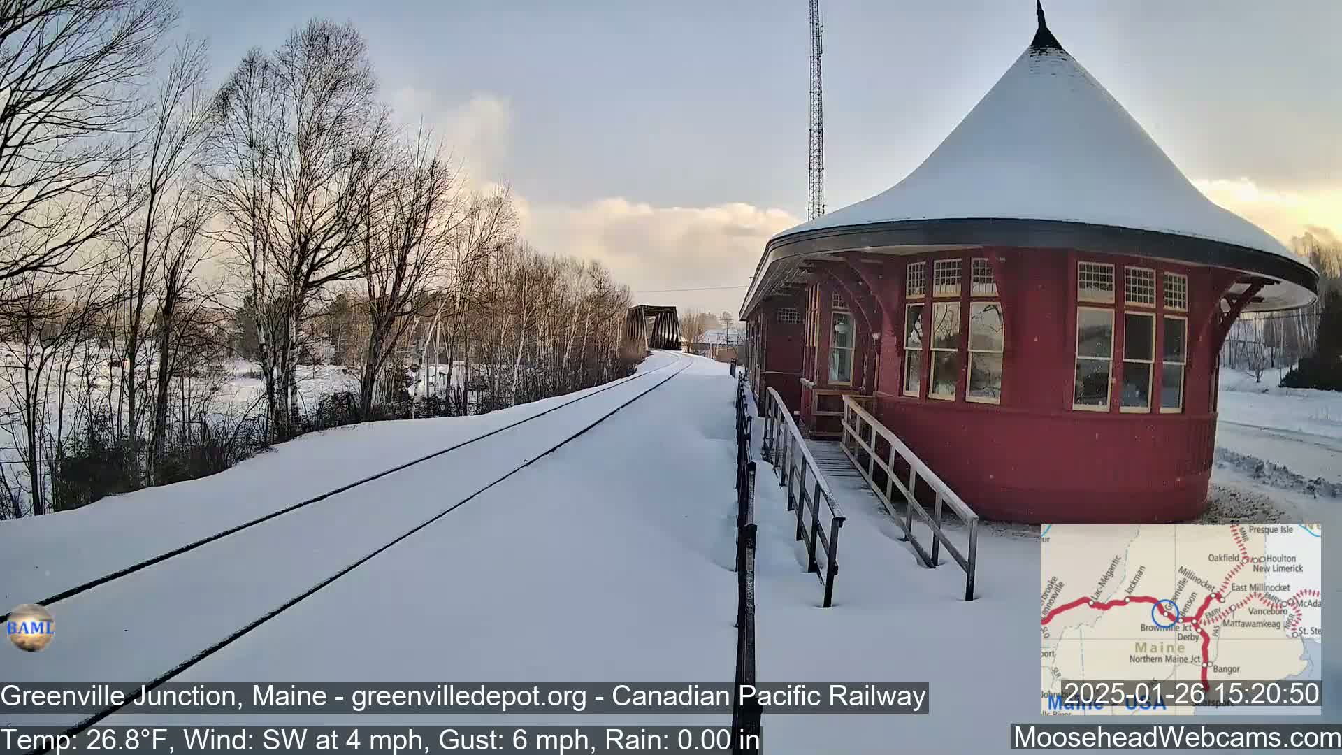 A snow-covered train depot sits beside a snow-covered railway track on a partly sunny day with a light southwest wind.