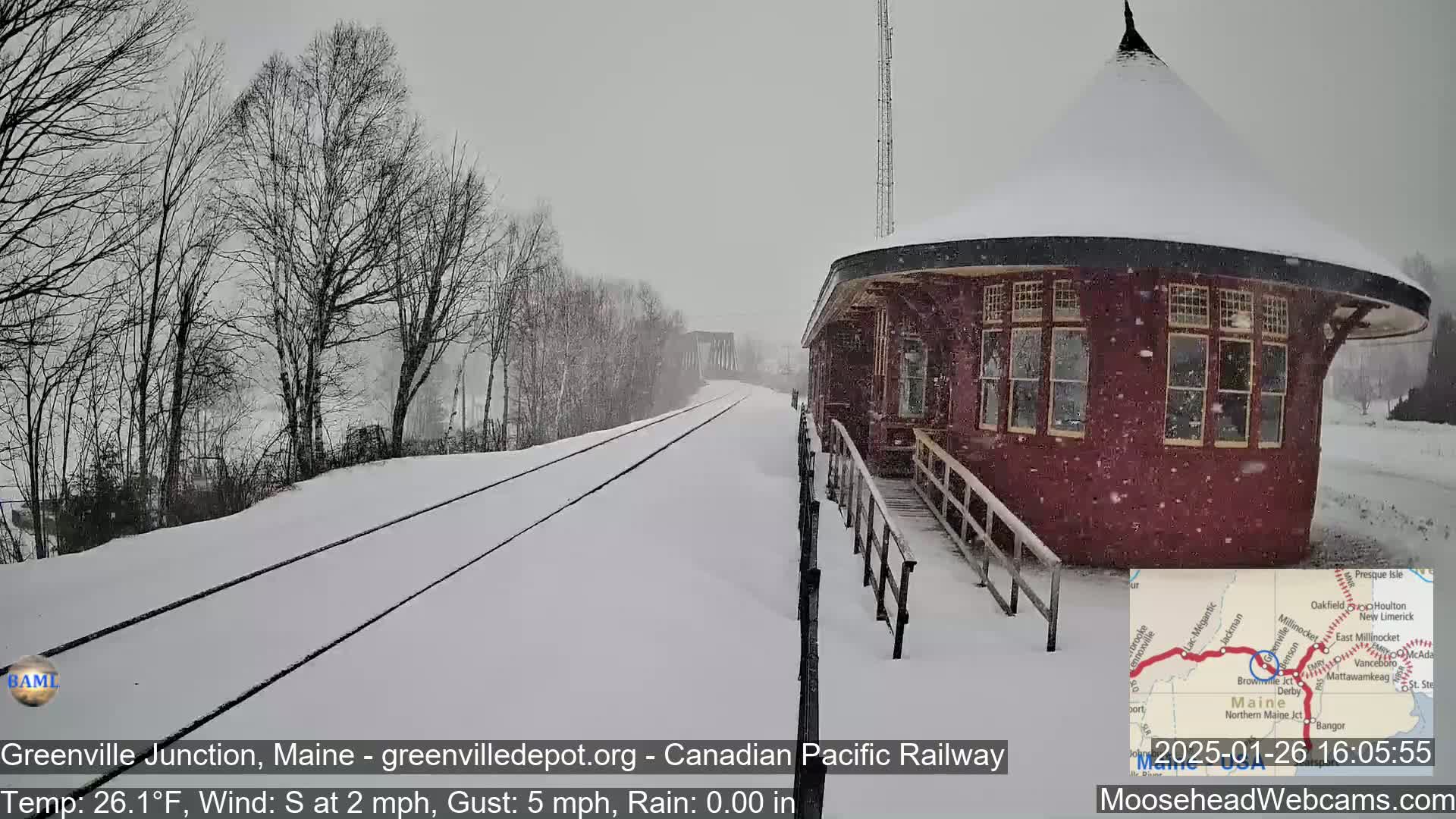 A snow-covered train depot sits next to a snow-covered railway track during a light snowfall.