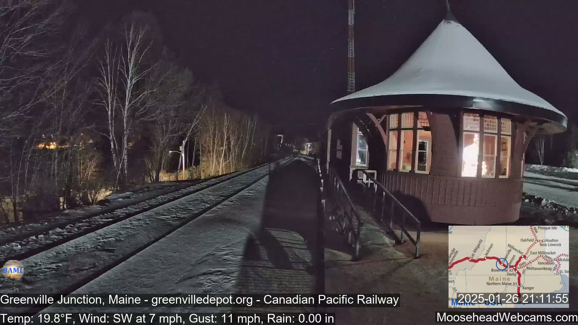 A snow-covered train platform with a small, illuminated building is visible at night under a dark sky.