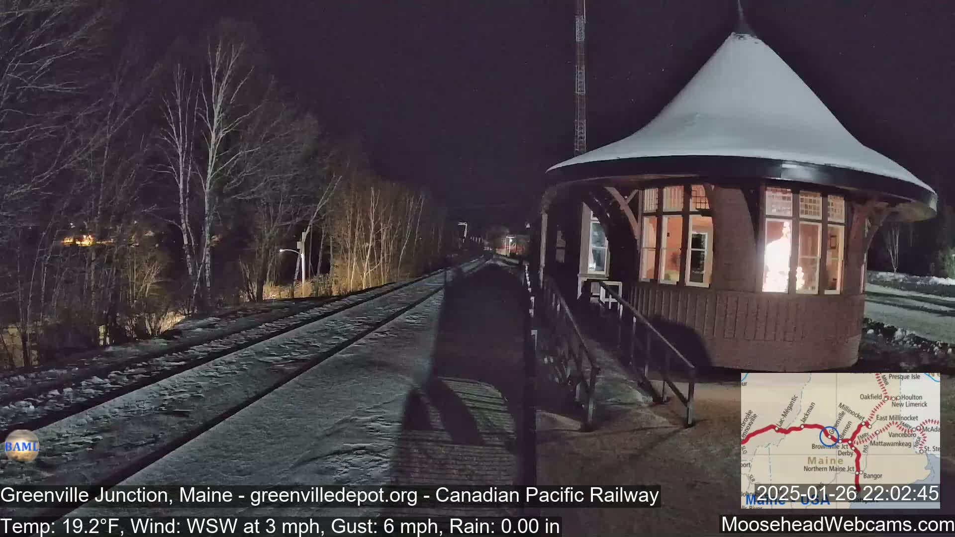 A snow-covered train depot at night, with a train track extending into the dark distance, under a clear sky.