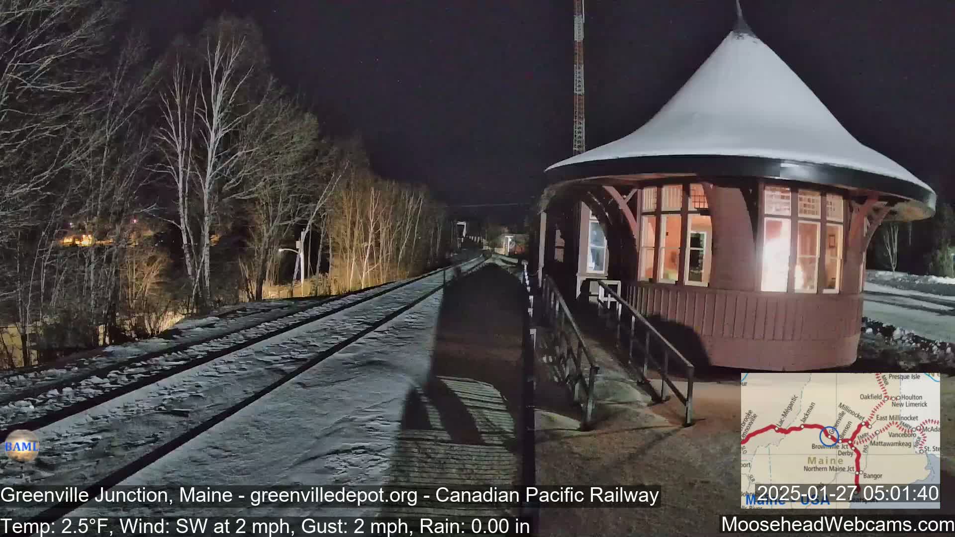 A snow-covered train platform and tracks are illuminated at night next to a round, snow-covered building.