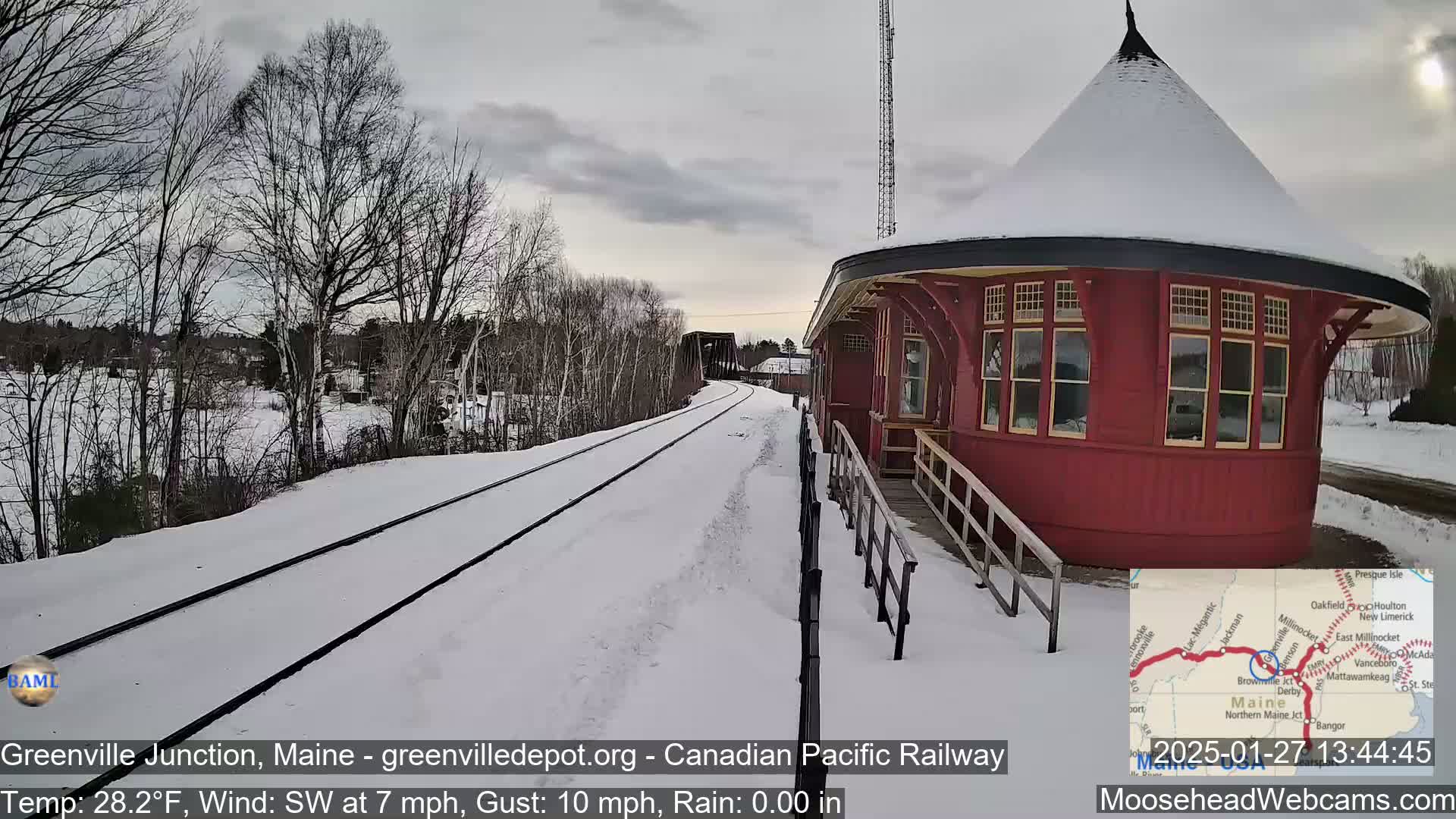 A snow-covered train track leads to a red, round train station under a cloudy sky.