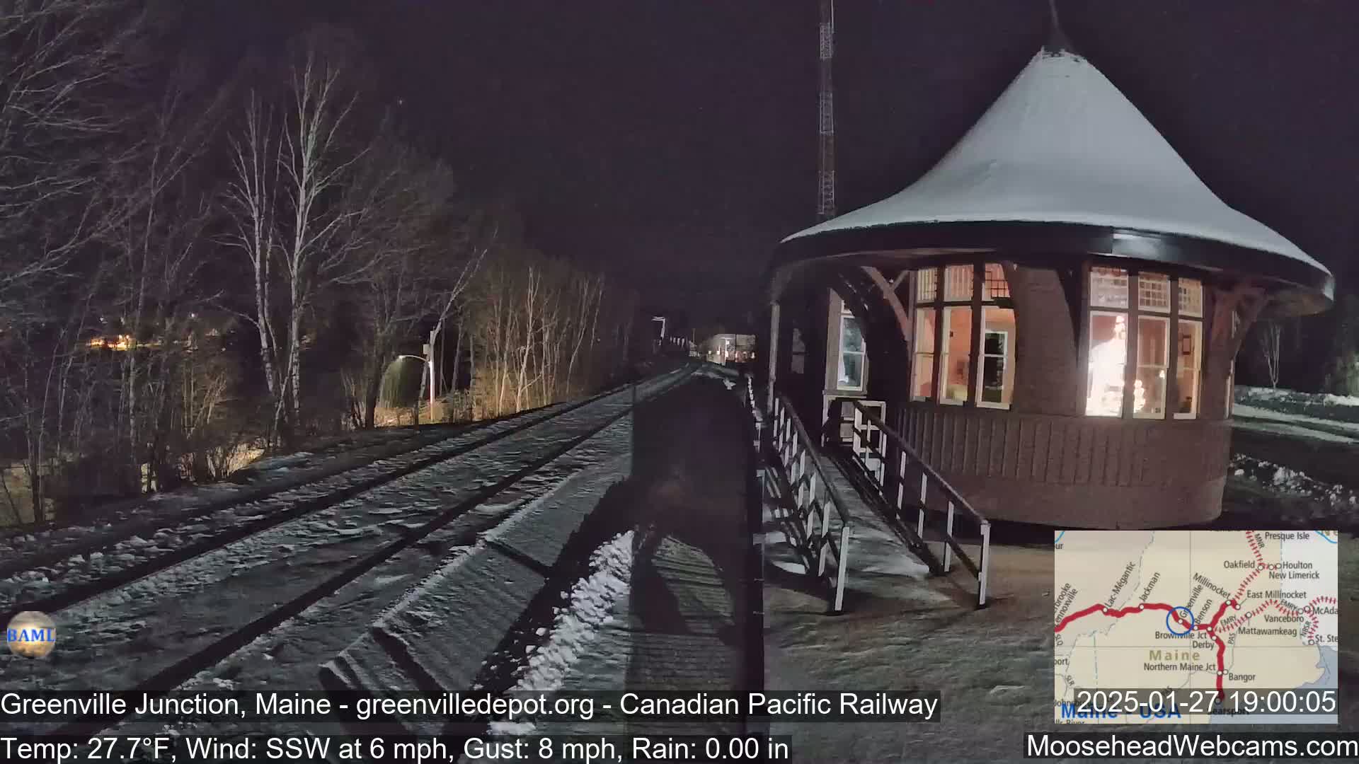 A snow-covered train platform and a small, illuminated building are visible at night, with a wind blowing from the south-southwest at 6 mph and gusts up to 8 mph.