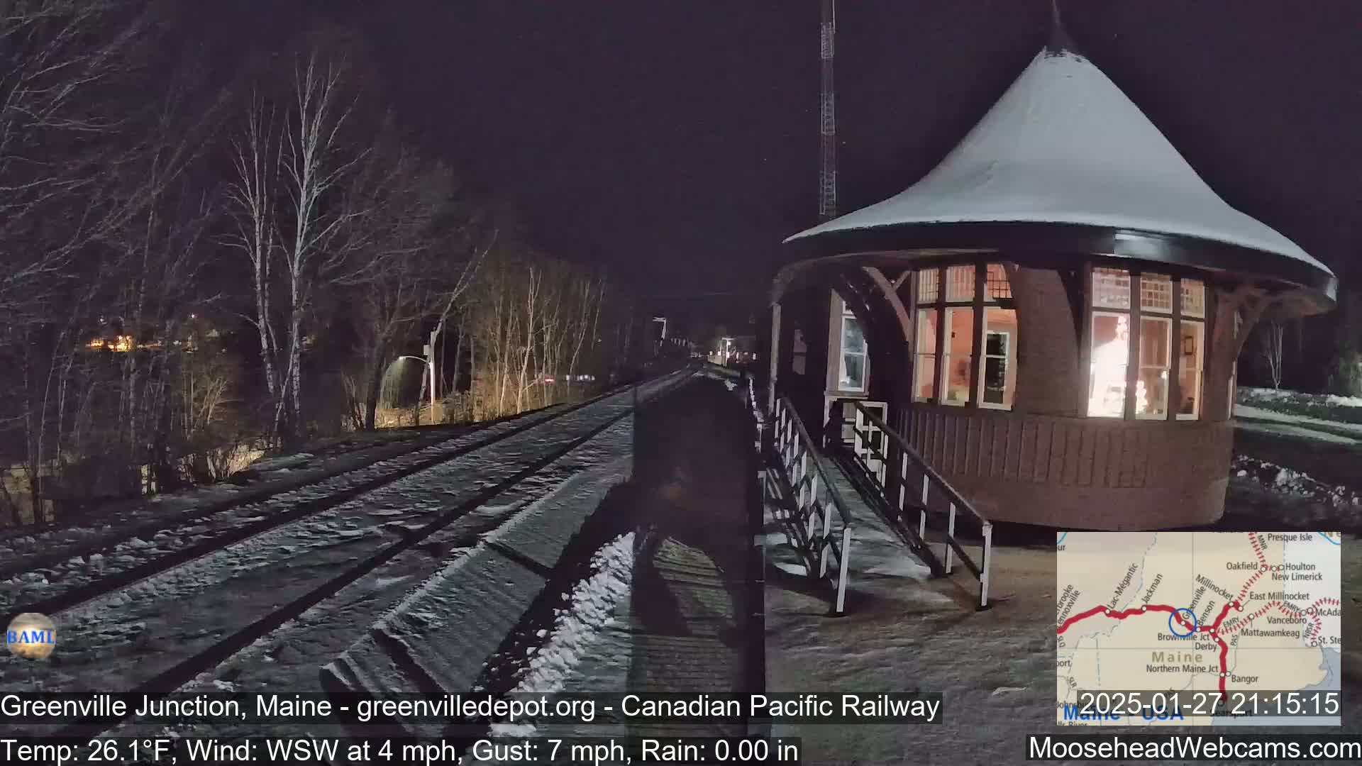 A snow-covered railway track leads to a lighted, snow-covered octagonal building at night, under a dark sky with a wind from the west-southwest at 4 mph and gusts to 7 mph.