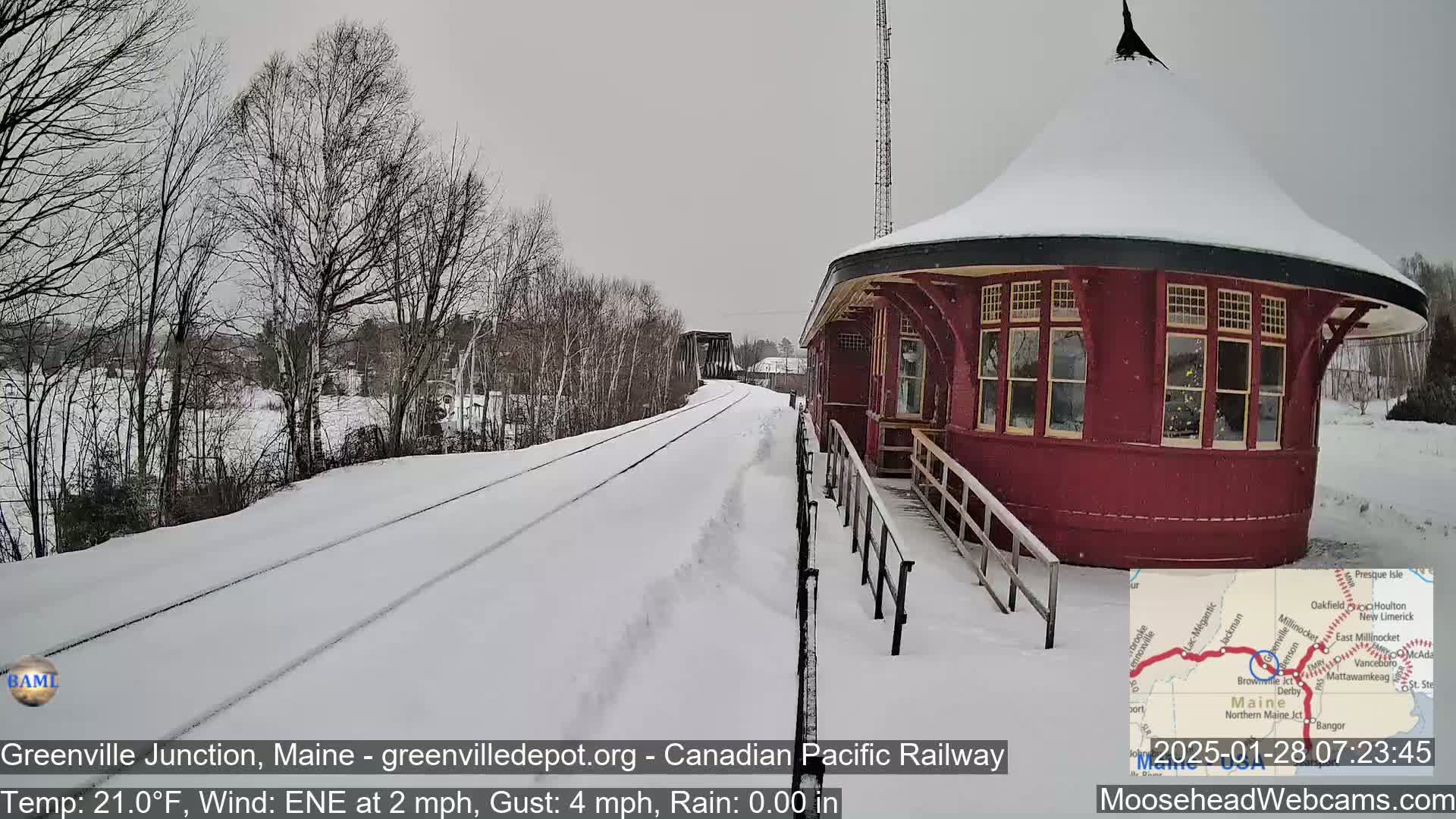 A snow-covered train platform with a red, round building is visible, with a railway track extending into the distance under a gray sky.
